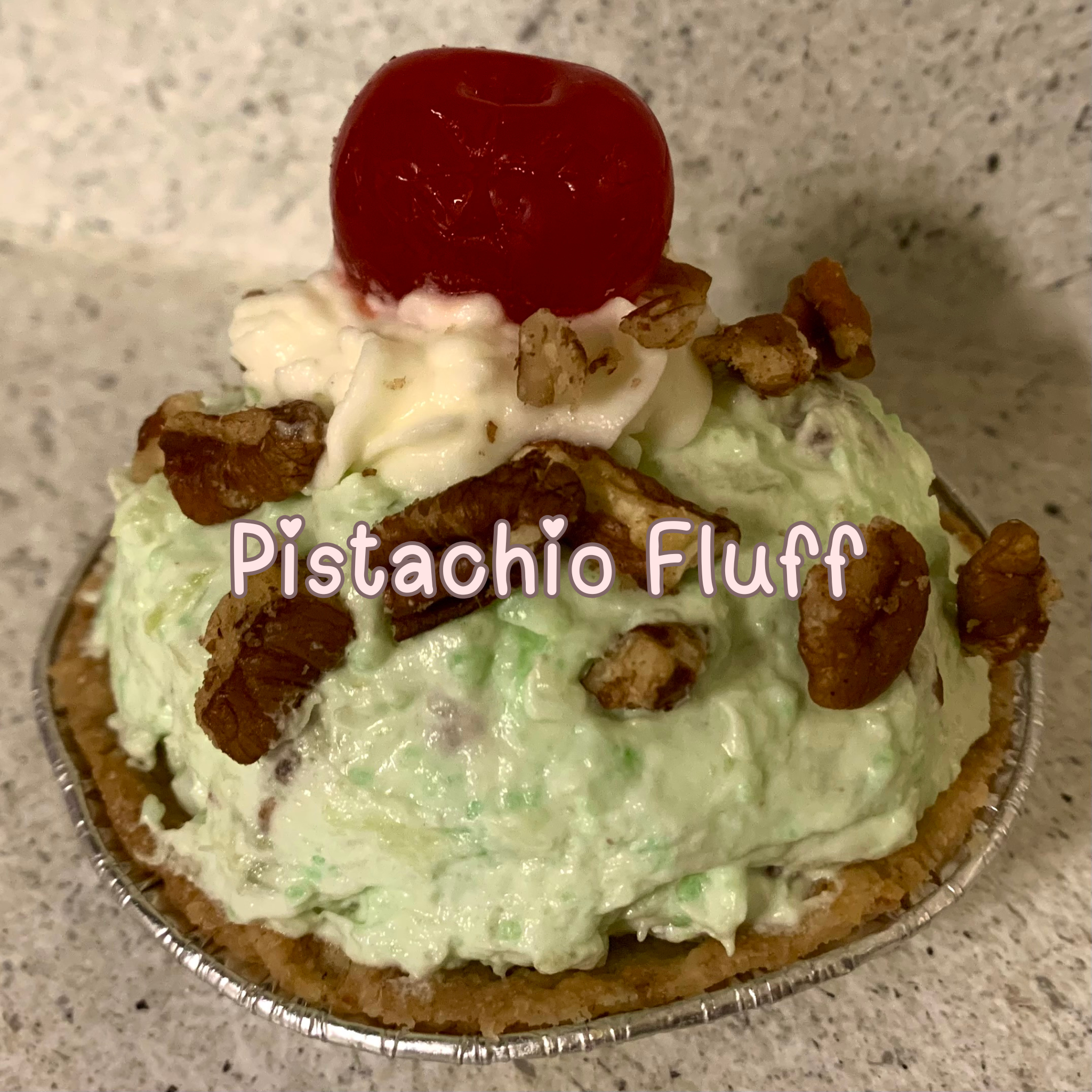 Mini pistachio fluff pie topped with whipped pistachio filling and chopped pecan, homemade whipped cream, and maraschino cherry garnishes.