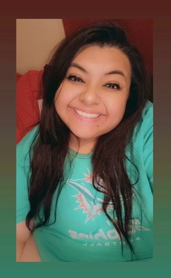 A young woman with long dark hair smiling and wearing a teal Miami Dolphins T-shirt.
