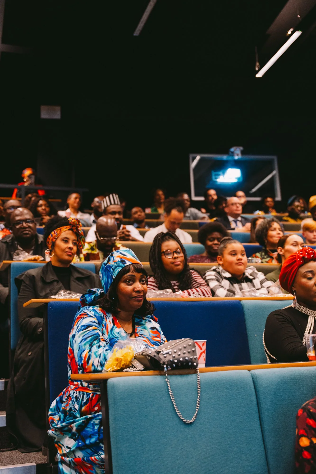 Audience seated in a theater or conference room, attentively listening to a presentation or speech.