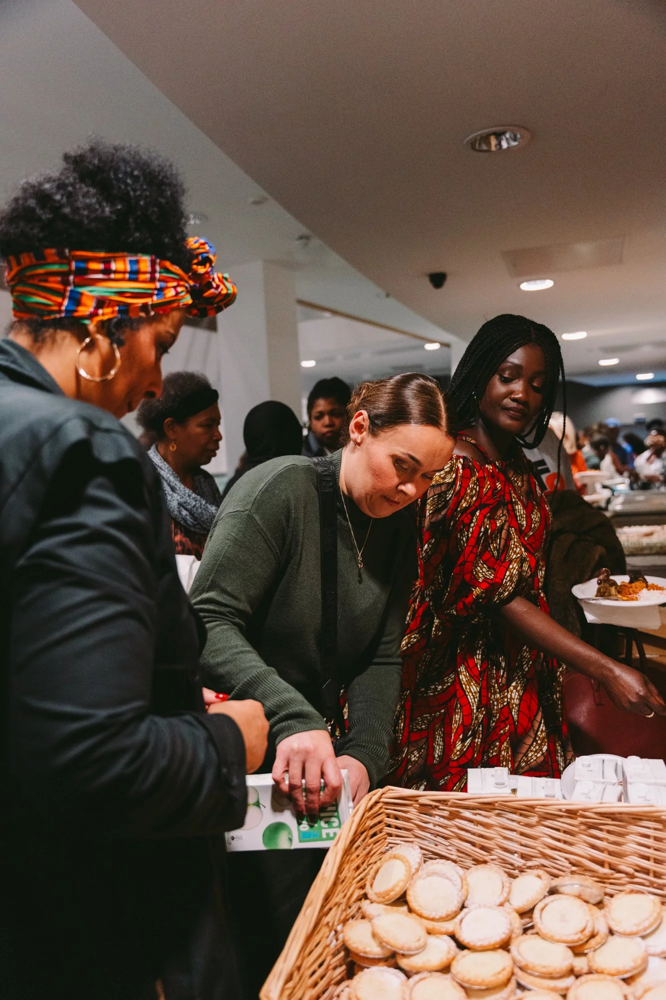 Women gather at a buffet table, serving themselves small cookies and food.