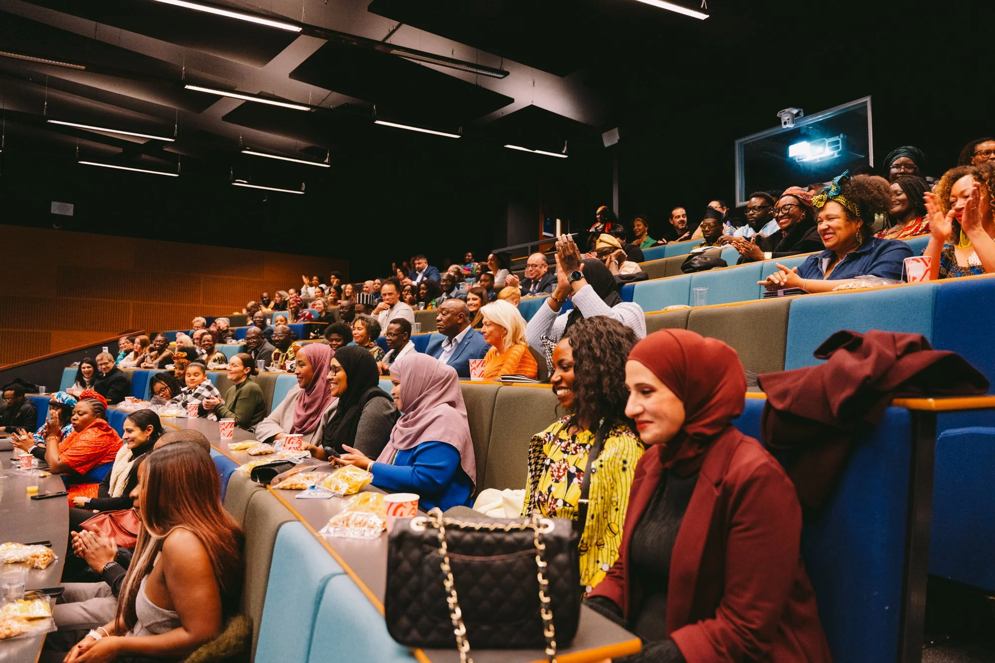 Audience members sitting in tiered auditorium seats, laughing and clapping during a live event or performance.