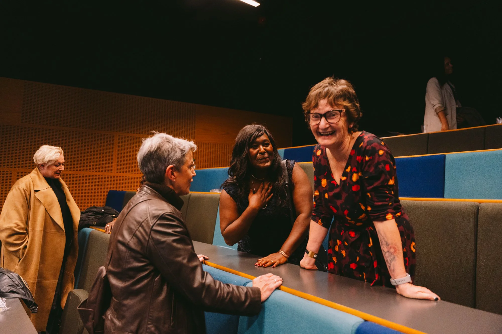 Group of diverse women conversing and laughing in an auditorium.