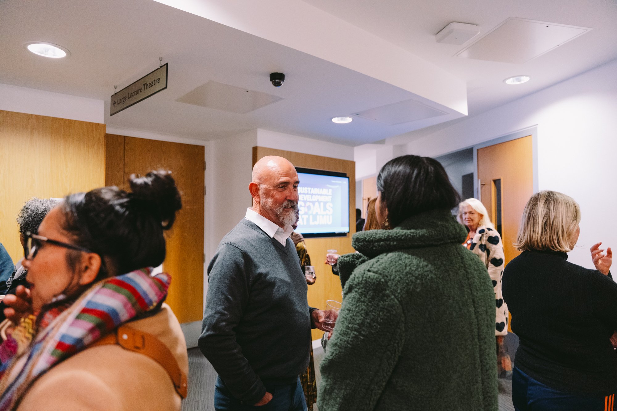 Group of people engaging in conversation at an indoor event, with a screen displaying 'Sustainable Goals' in the background.