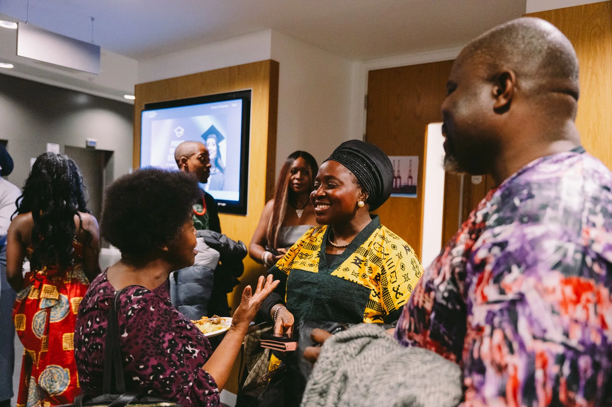A group of diverse people socializing at an indoor event, with some smiling and engaging in conversation.