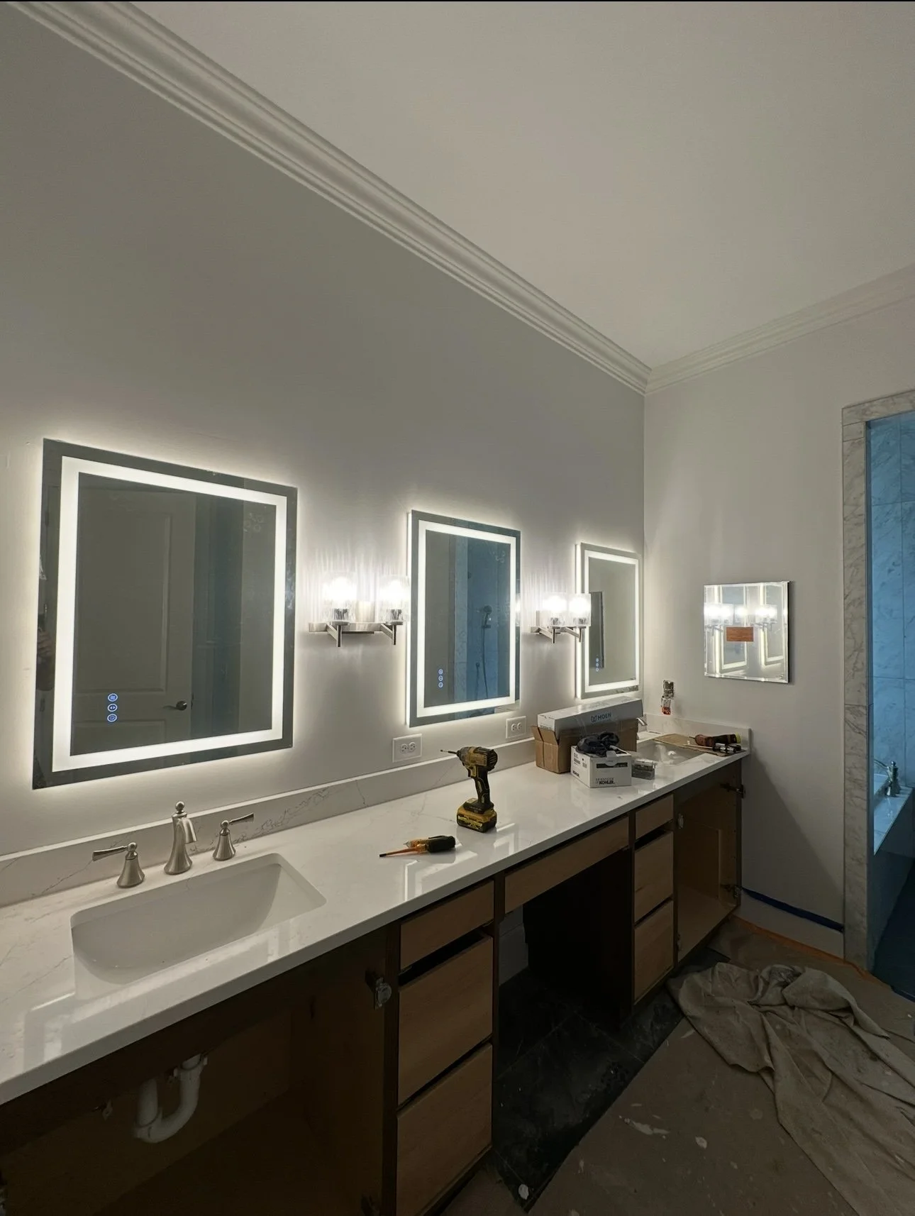 Bathroom vanity area with three illuminated mirrors, a sink, and construction tools on the countertop.