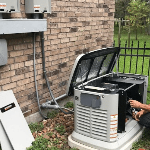 Technician servicing an air conditioning unit outside a brick building, with a black fence and green grass in the background.