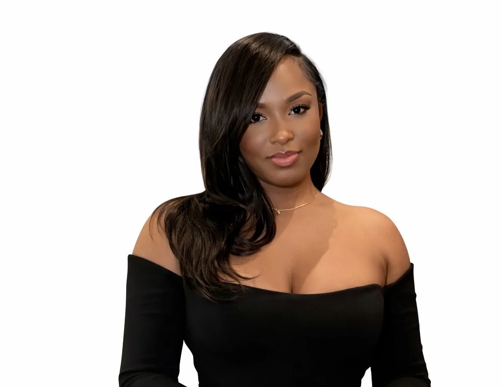 Portrait of a woman with long dark hair, wearing an off-the-shoulder black top, standing against a plain white background.