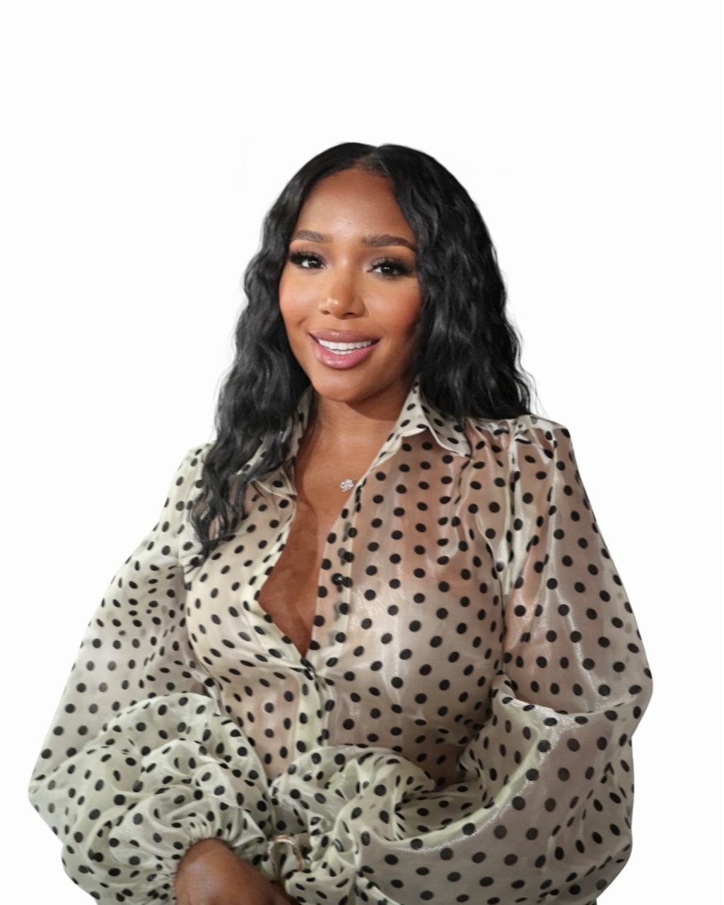 A woman with long wavy black hair smiling, wearing a beige polka dot blouse with puffy sleeves, against a plain white background.