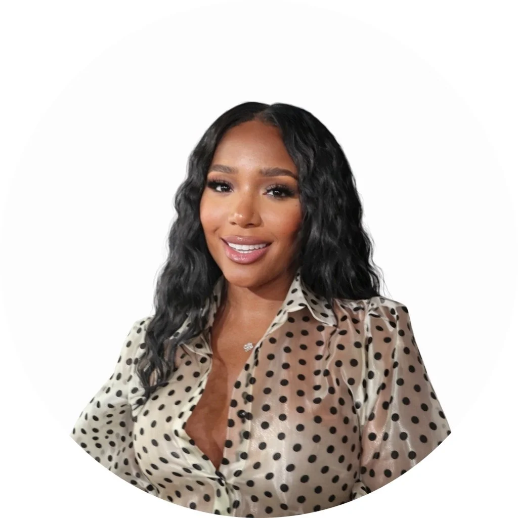 A woman with long, wavy black hair smiling, wearing a beige polka dot blouse.