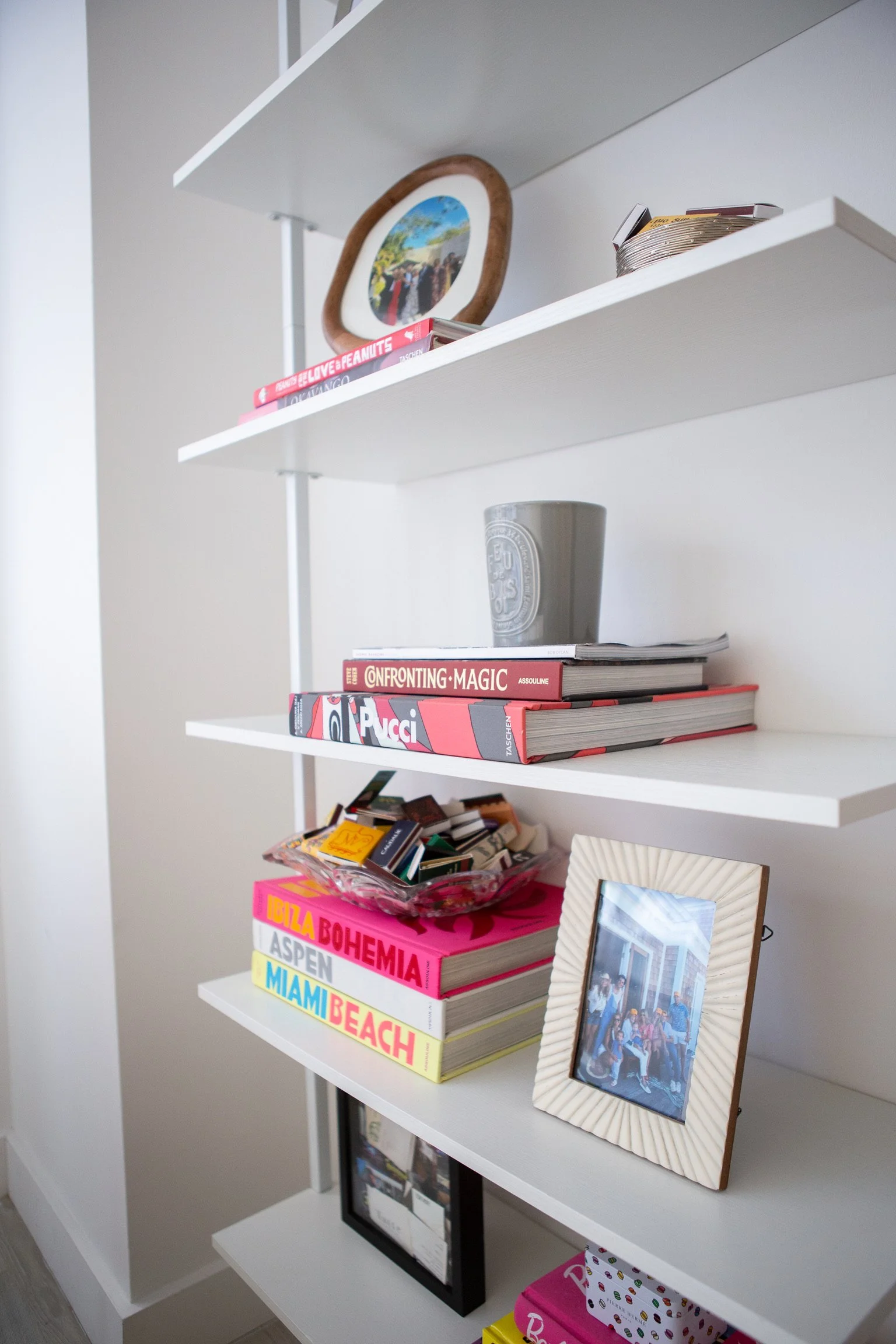 A white shelf filled with colorful books and several framed photographs.