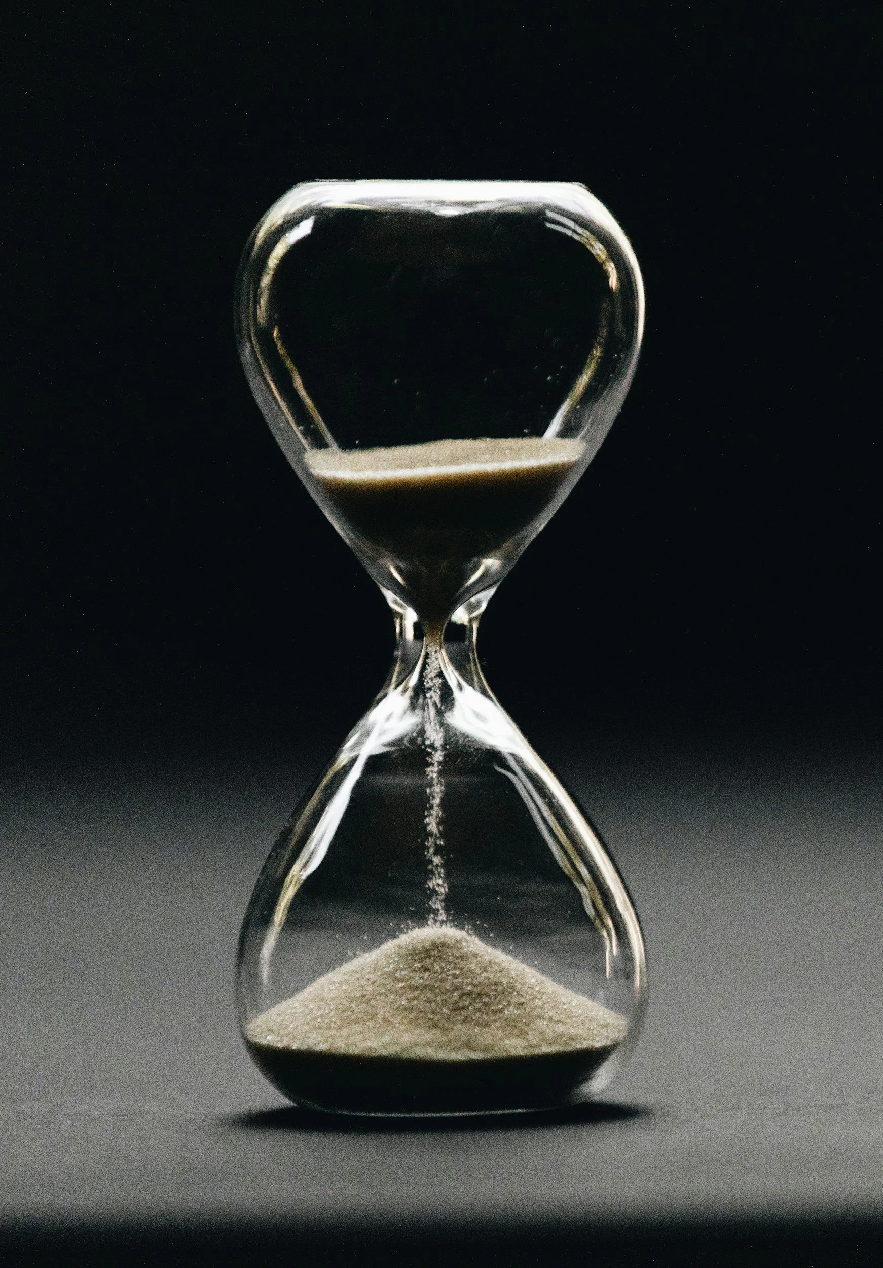 An hourglass with black sand inside, against a dark background.