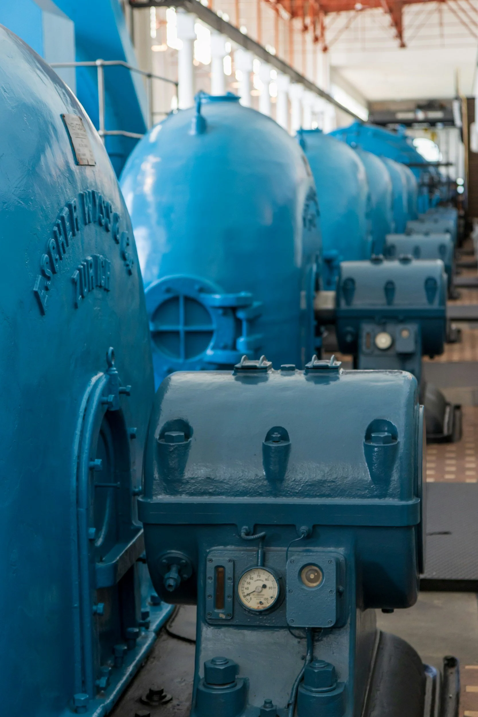 Row of large blue industrial tanks or machinery in a factory setting.