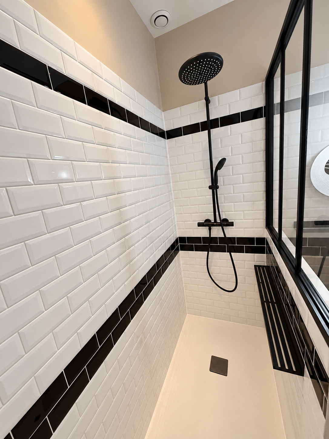 Douche rénovée à Malakoff avec carrelage métro blanc, frises noires, colonne de douche noire et paroi vitrée.