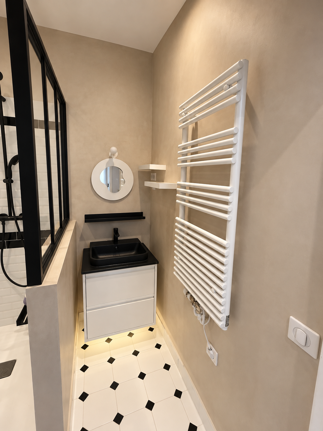 Meuble vasque suspendu avec lavabo noir, miroir rond et sèche-serviettes dans une salle de bain rénovée à Malakoff.
