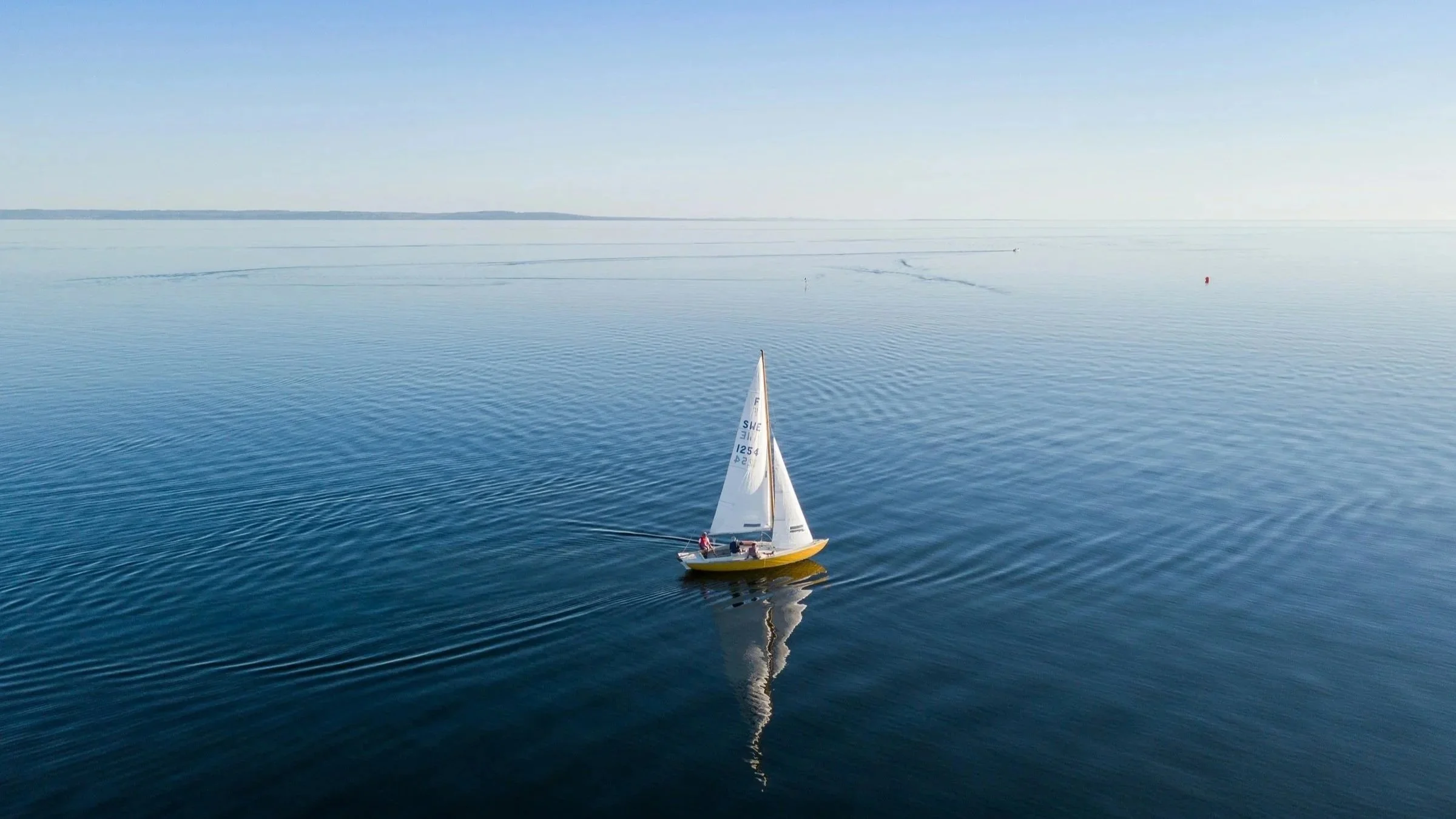 A marina at sunset with numerous docked boats and yachts, some with tall masts, wooden pilings in the water, and a sky with scattered clouds.