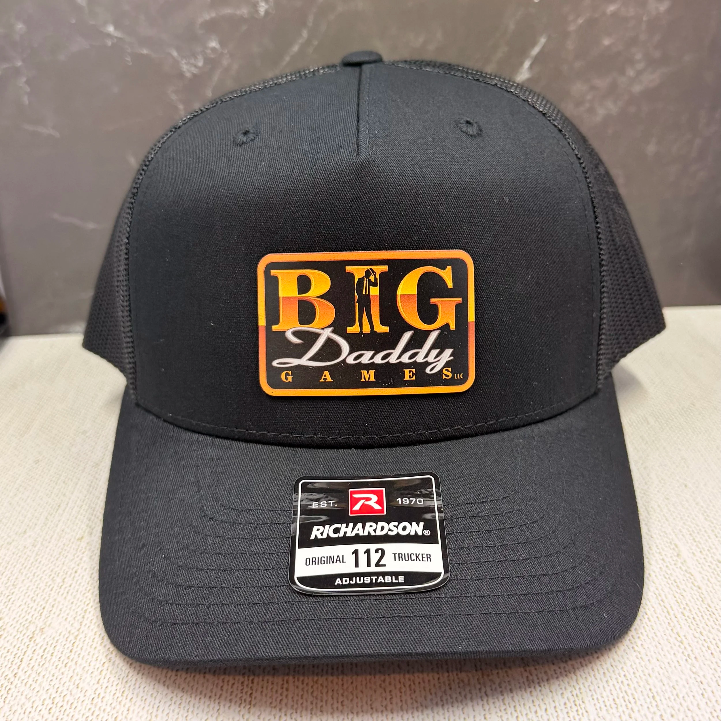 Close-up of a black trucker cap with a 'Big Daddy Gaming' logo, displaying a sticker indicating the cap is an original model, size 112, adjustable, and made by Richardson.