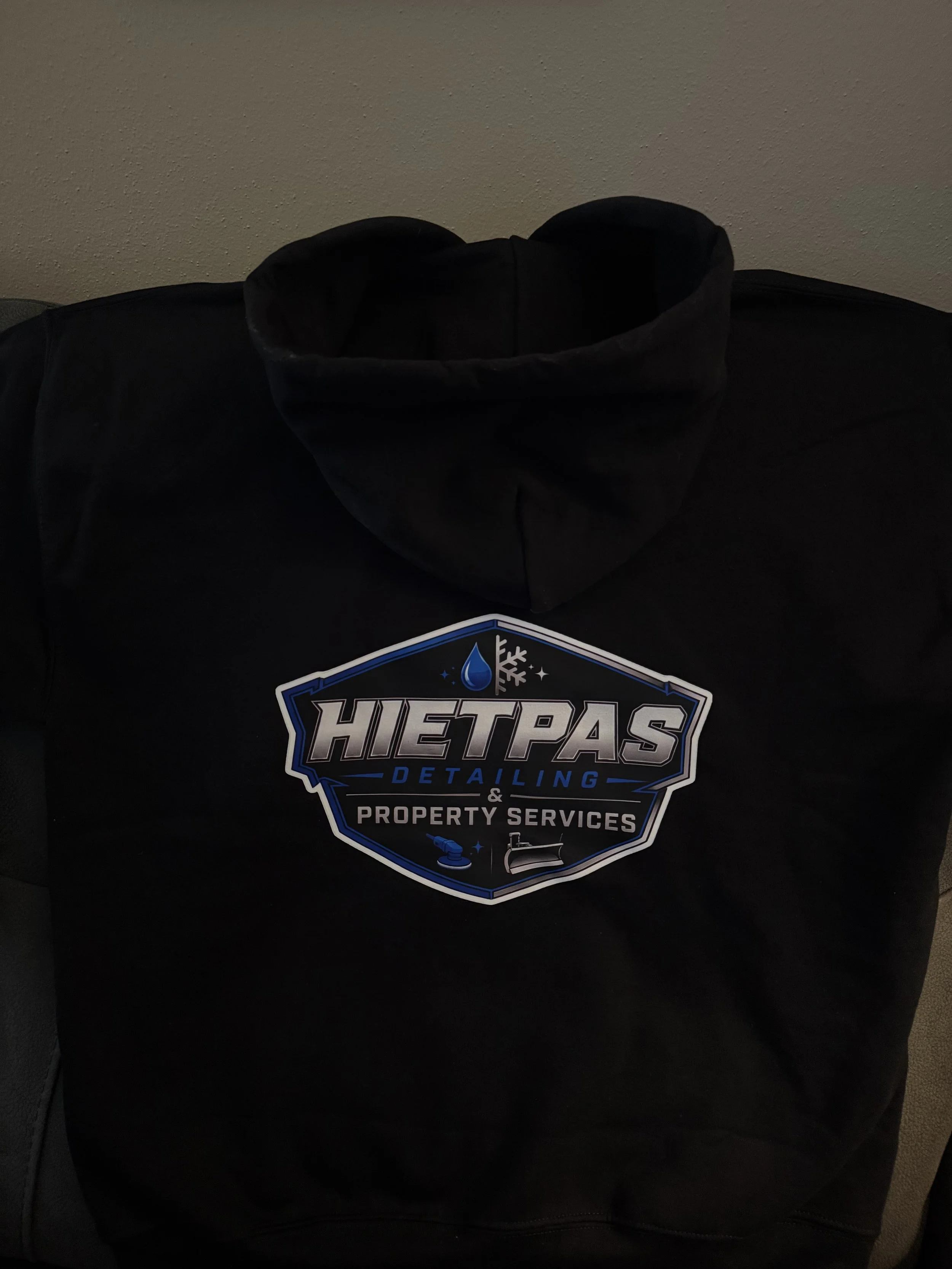 Back view of a custom black hoodie showing a large, detailed DTF printed shield logo for Hietpas Detailing & Property Services.