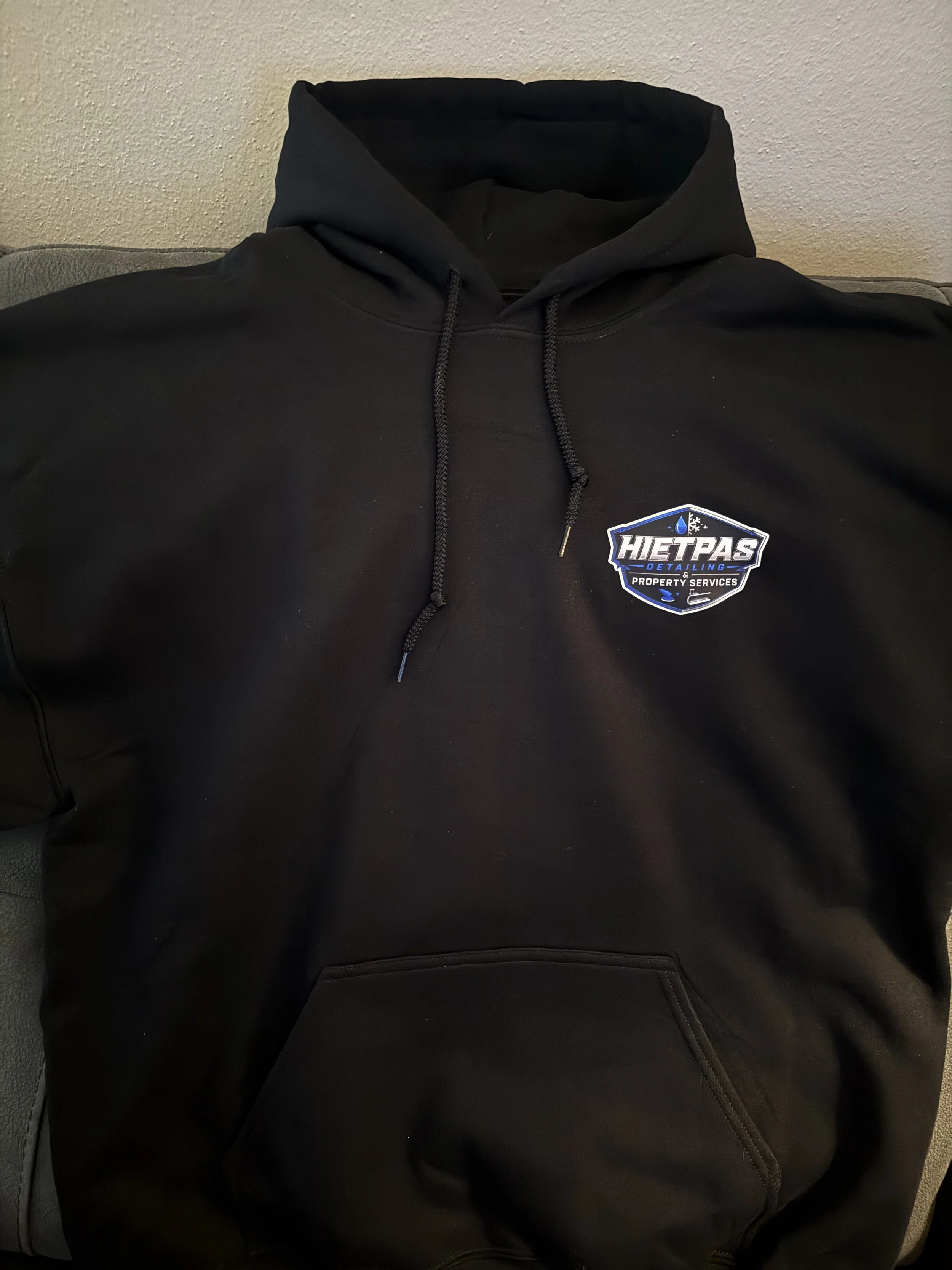 Front view of a custom black pullover hoodie featuring a left-chest DTF printed logo for Hietpas Detailing & Property Services.