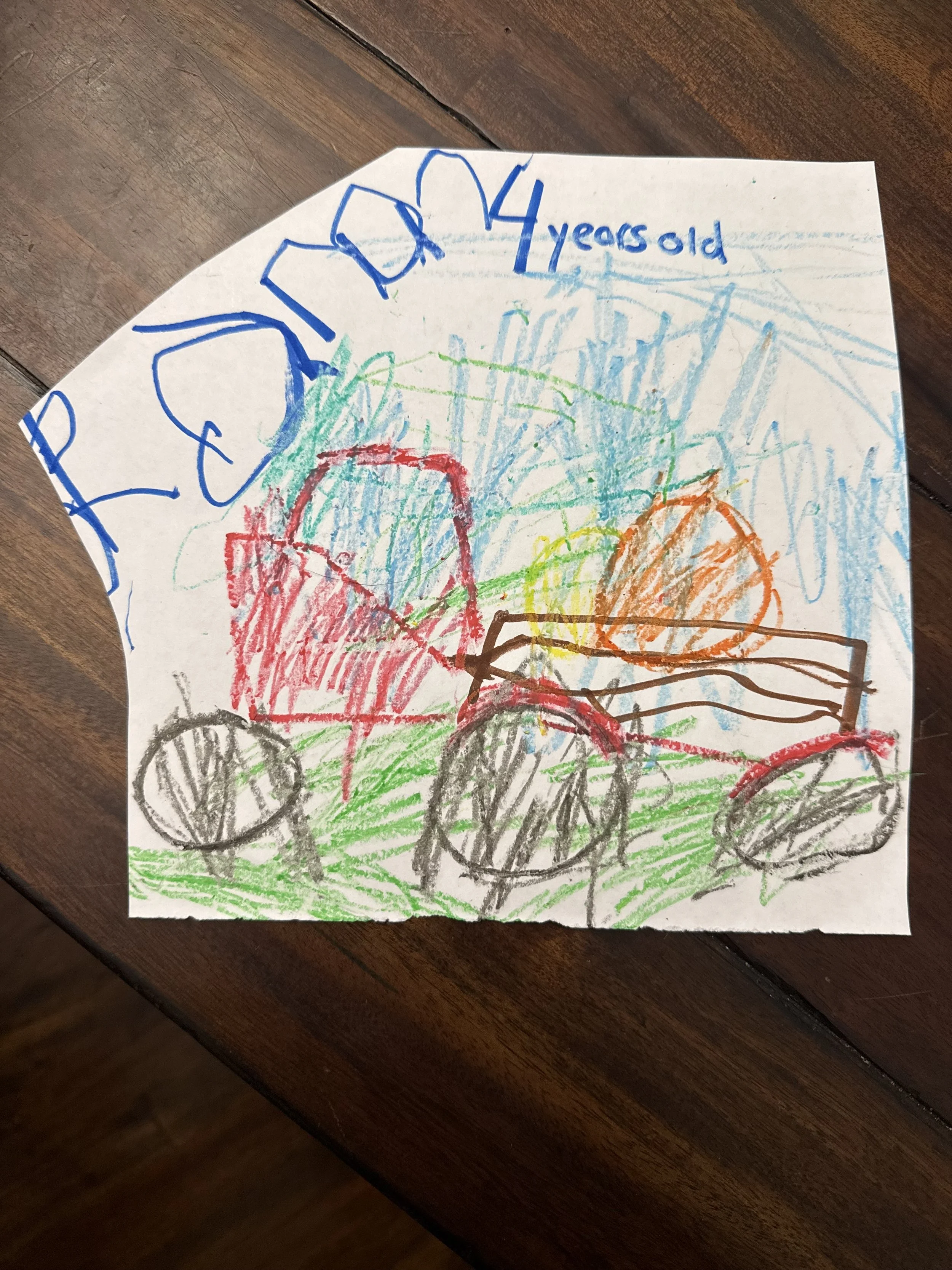 Child's colorful crayon drawing of a vehicle with big wheels, trees, and a blue sky, with the words 'POPOUX 4 years old' written on top.