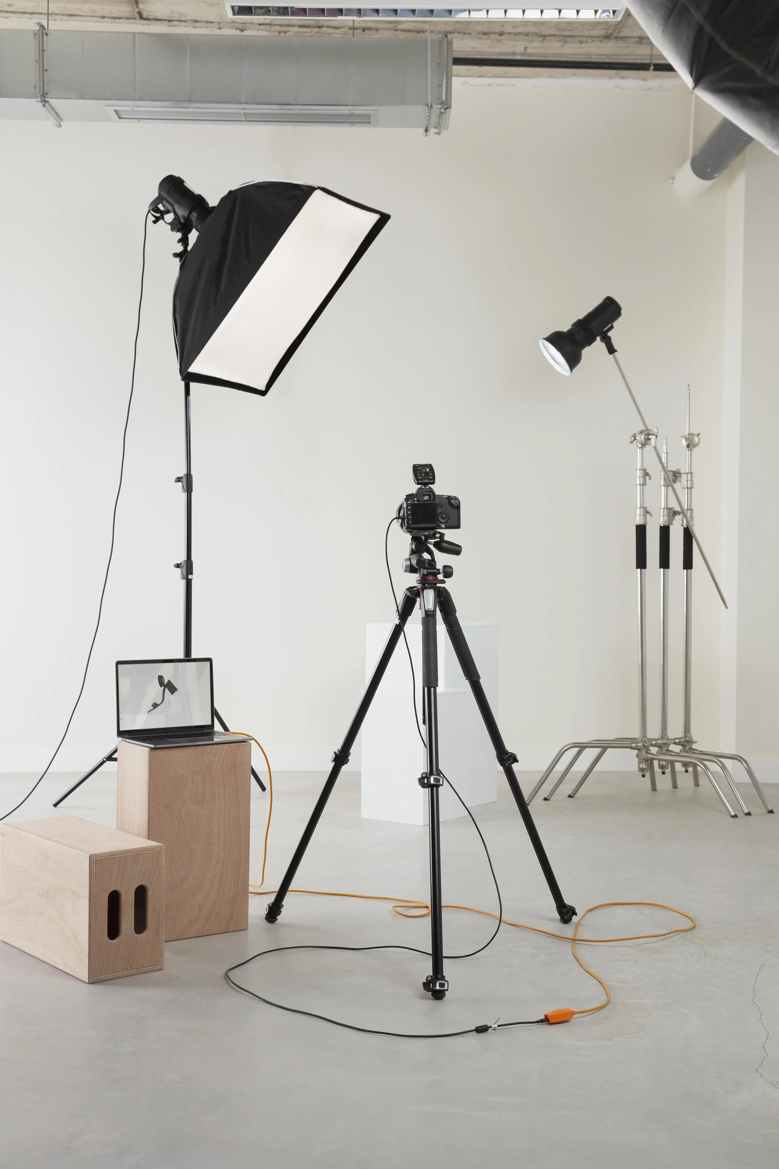 Photography studio setup with lighting, camera, and backdrop equipment on a plain indoor background.