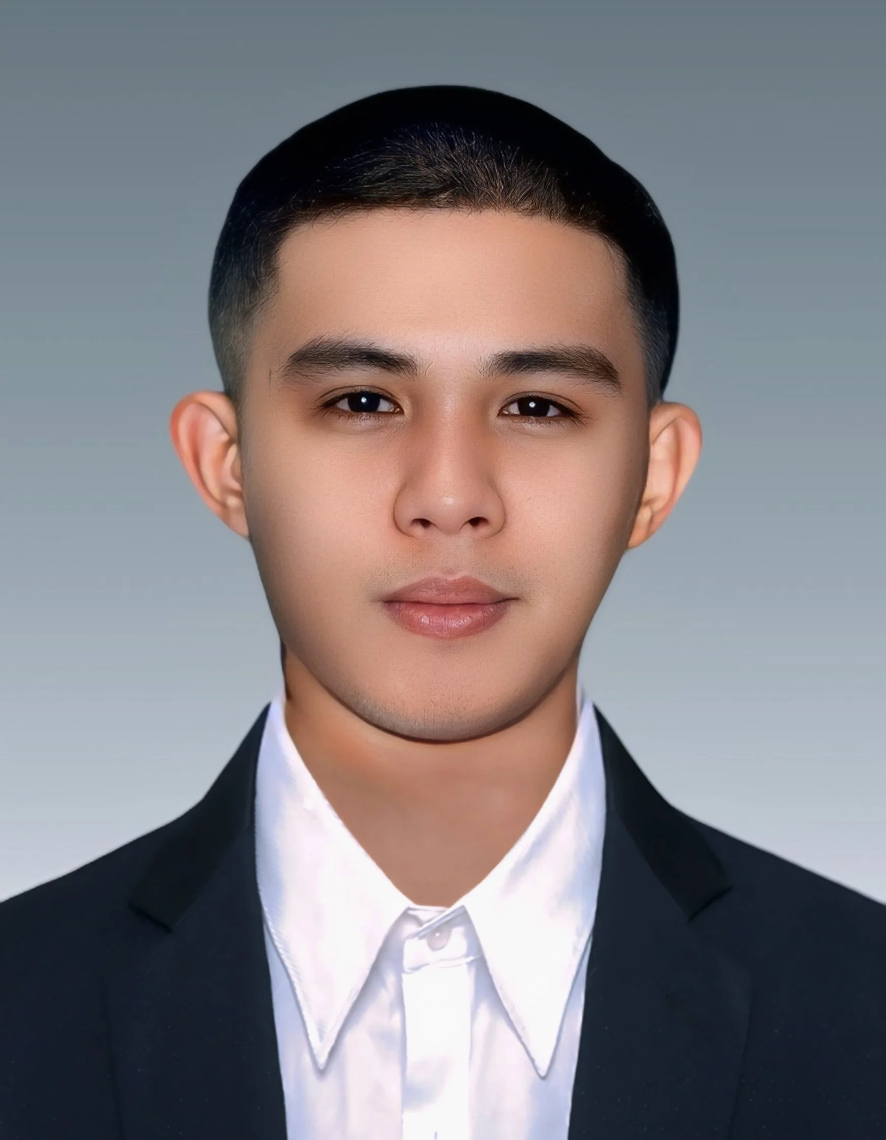 Young man in a black suit and white dress shirt, facing forward with neutral expression, against a plain background.