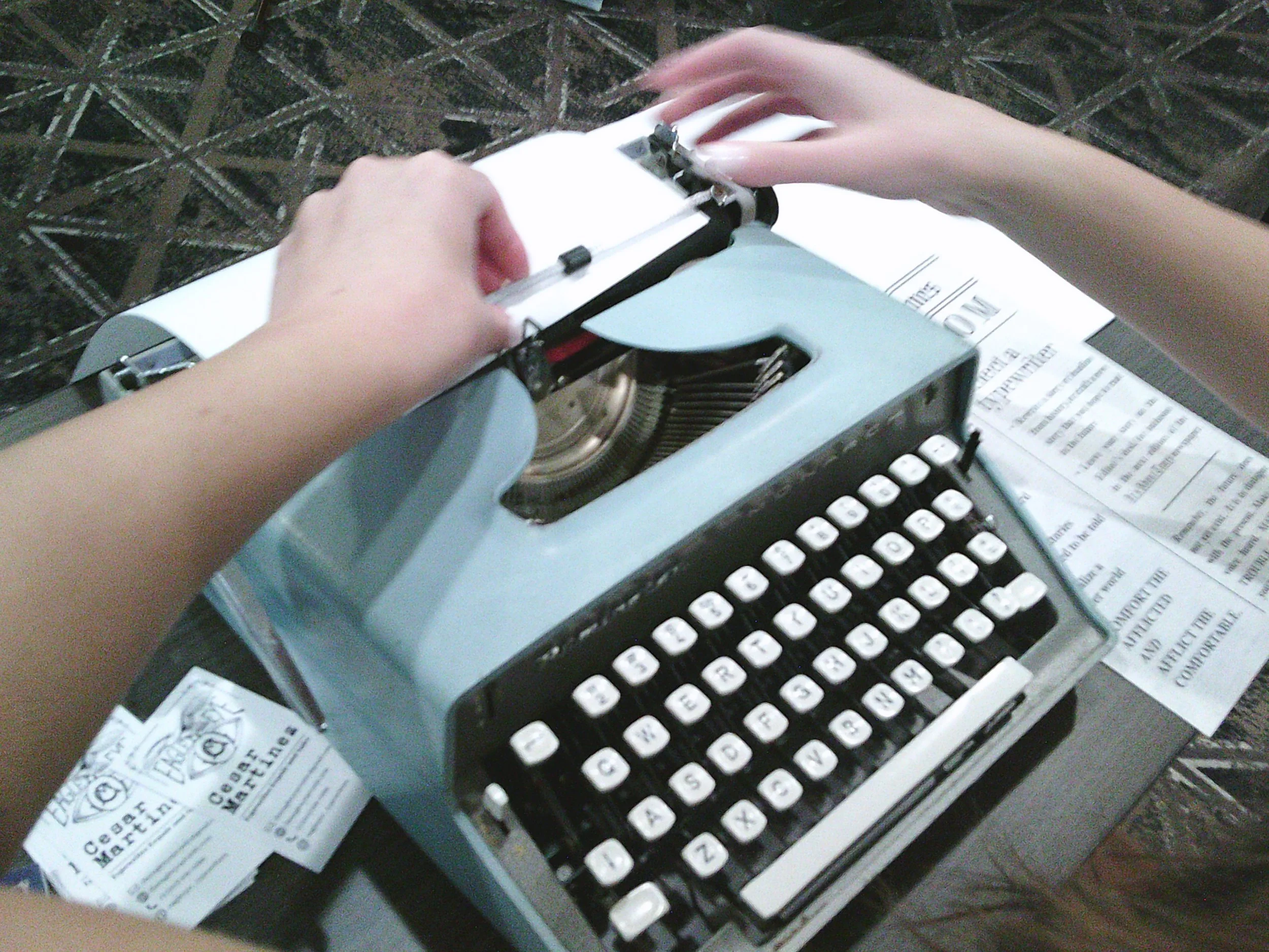 Person typing on a vintage blue typewriter with papers underneath.