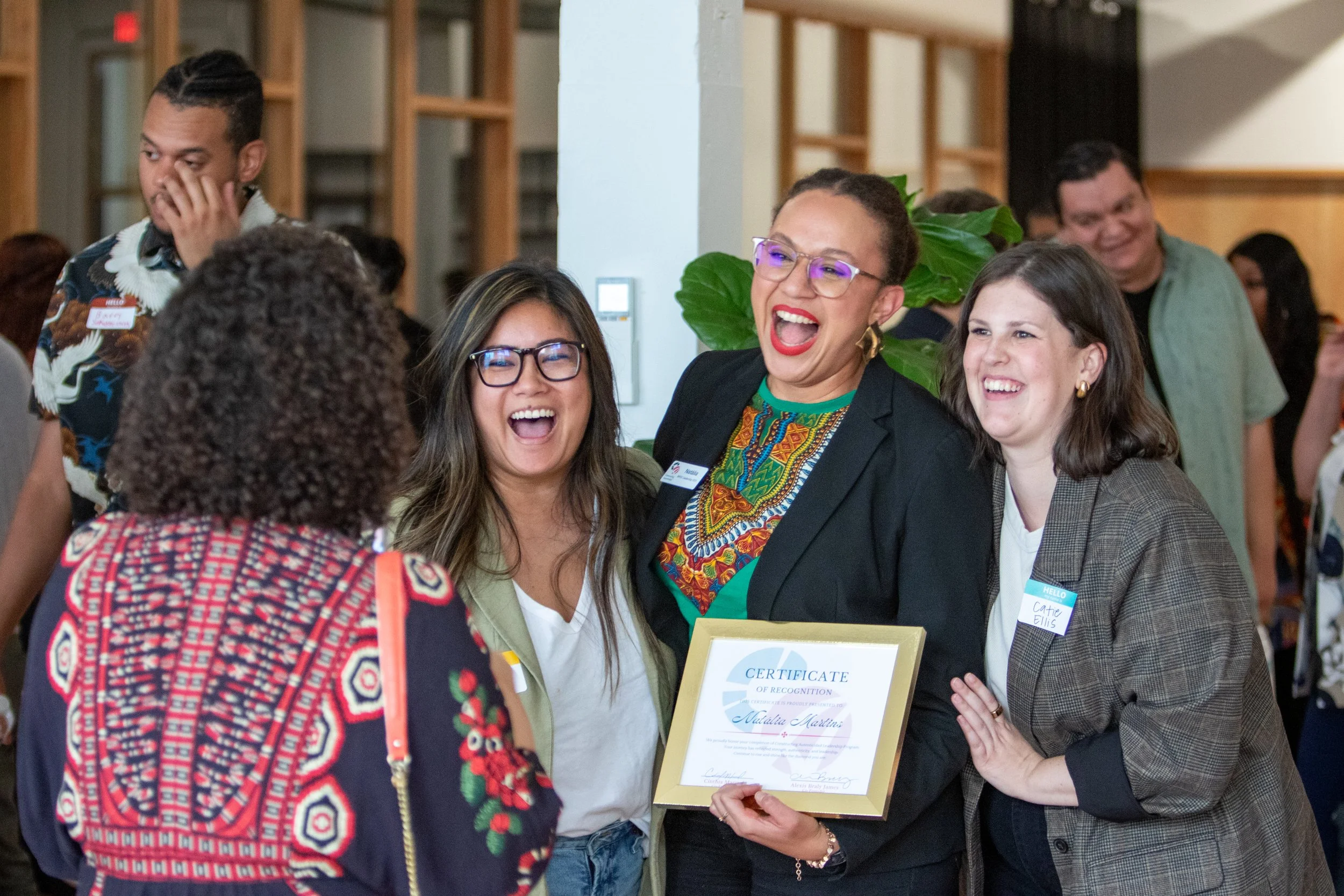 Group of people at an award ceremony, with three women smiling and holding a certificate, celebrating together.