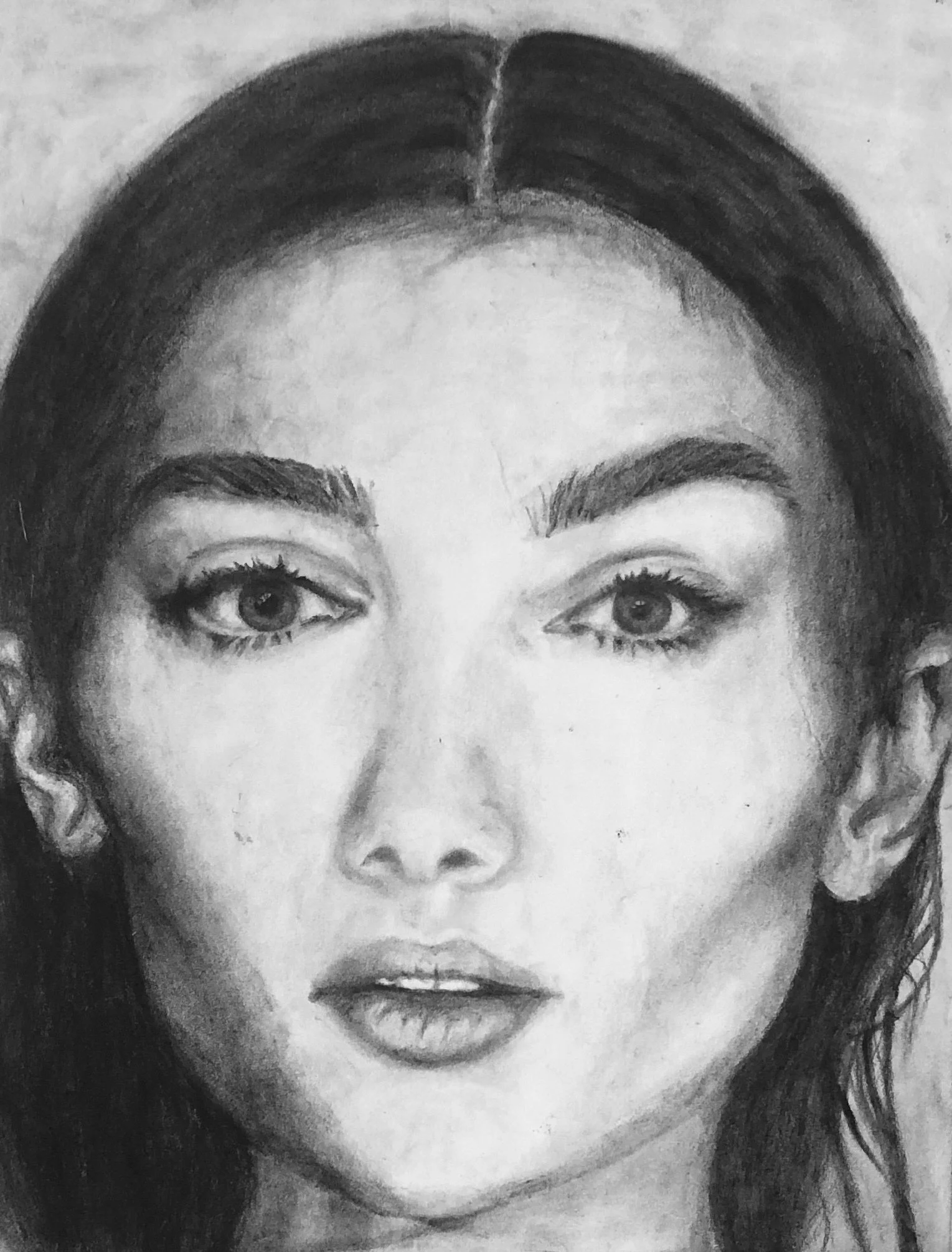 A detailed charcoal drawing of a woman's face with dark hair, prominent eyebrows, and expressive eyes.