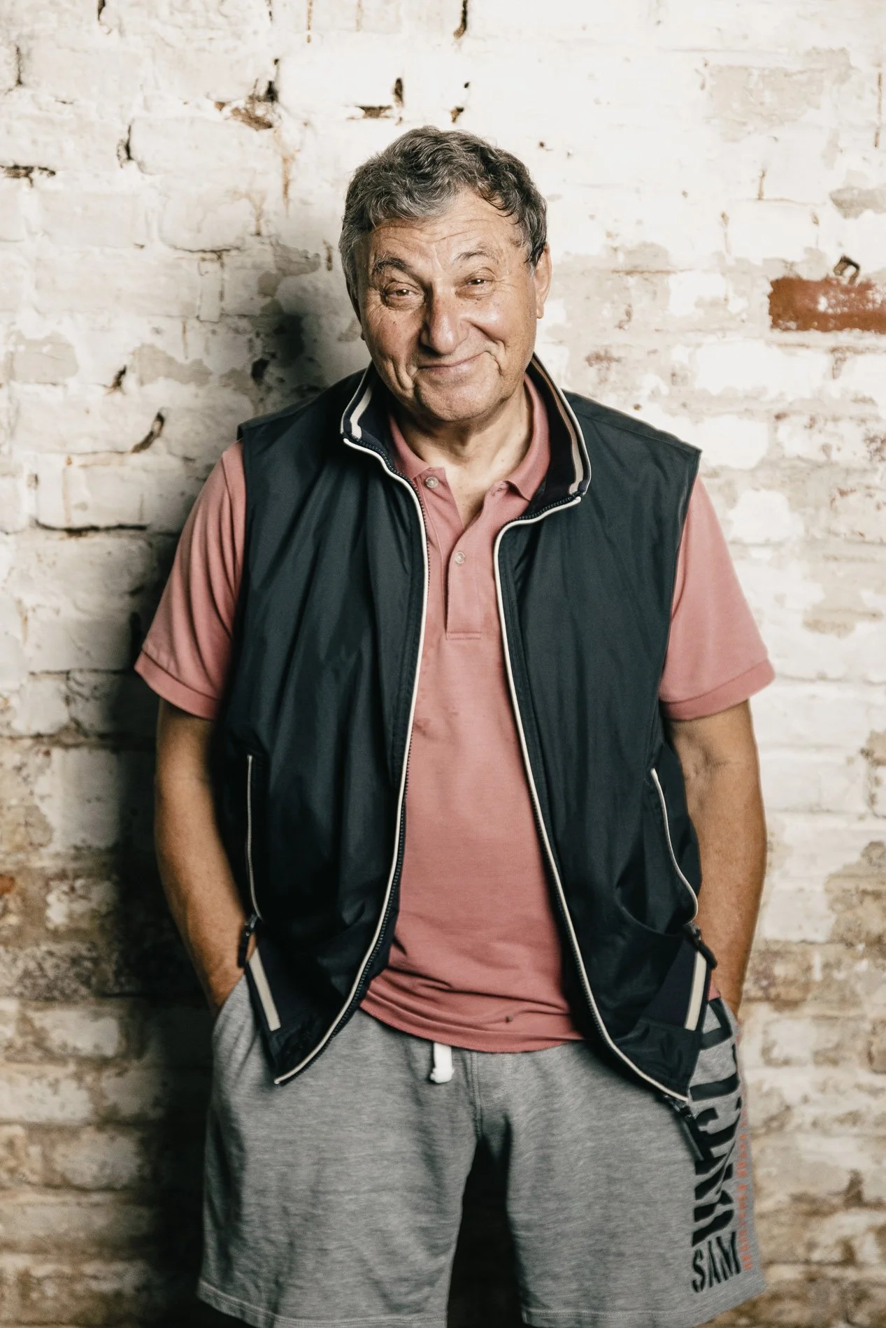 Ein älterer Mann, der lächelt, vor einer weißen Ziegelwand.