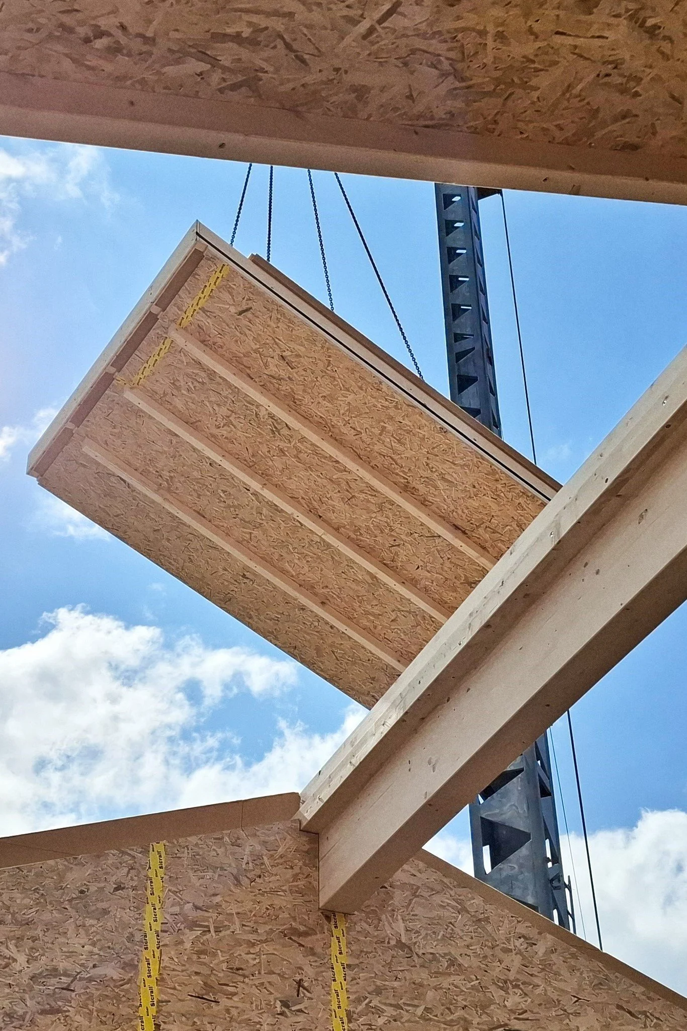 Ein Holzelement hängt an Seilen in der Luft. Im HIntergrund ist der Blaue HImmel zu sehen.