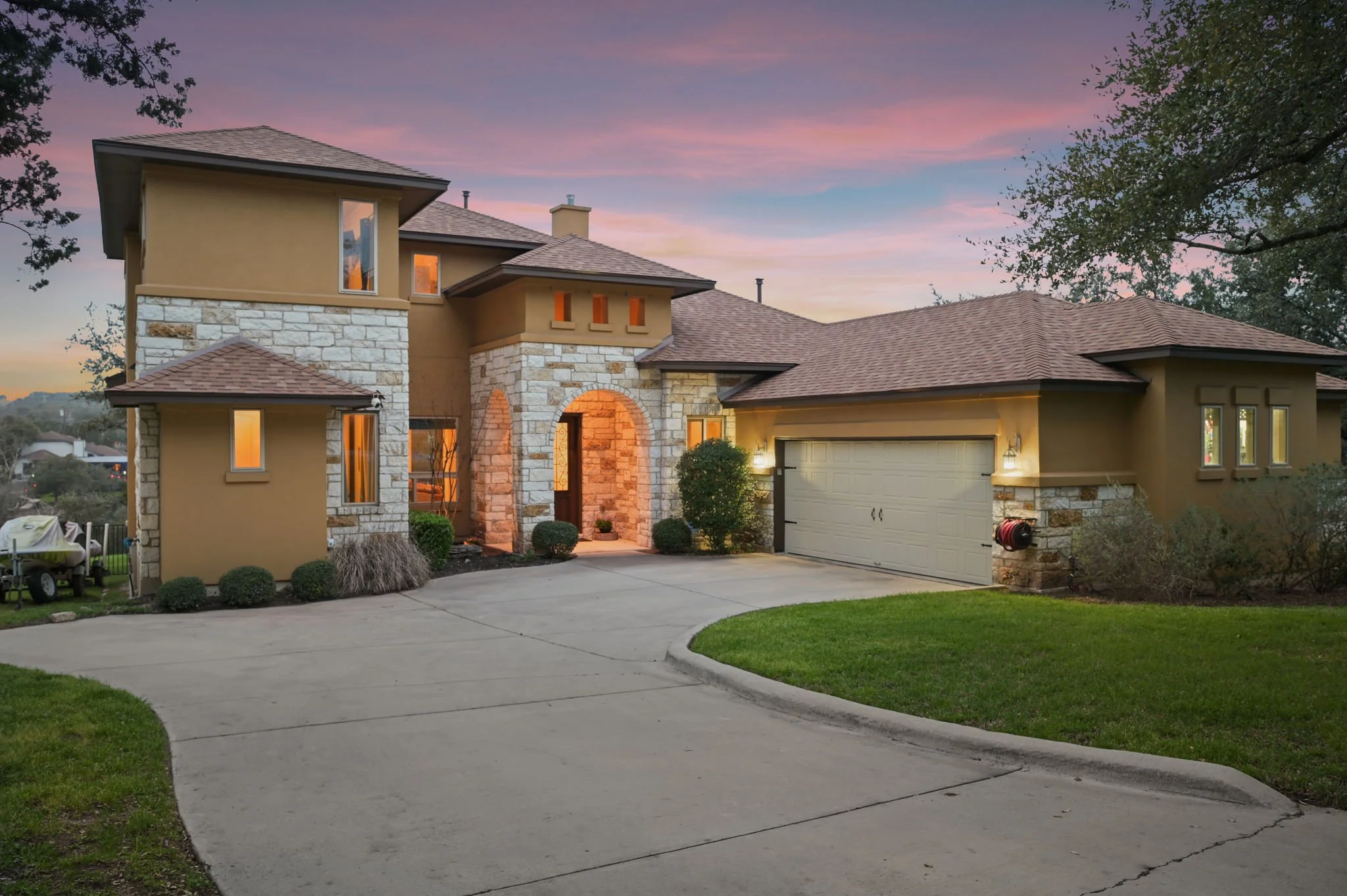 Front view of a two-story house with a stone and stucco exterior, a garage, and a driveway, during dusk with a colorful sky.