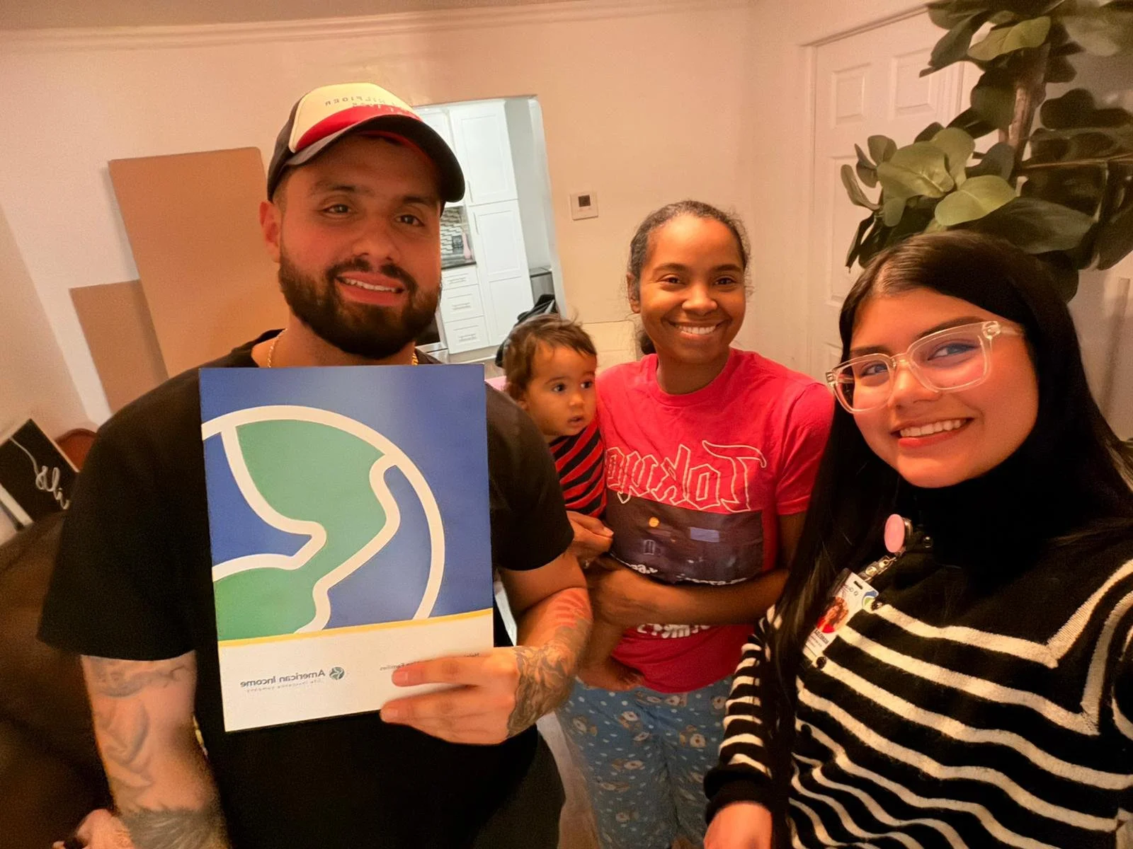 Un grupo de cuatro personas (dos mujeres, un hombre y un niño) sonrientes en una reunión en interiores, con un hombre sosteniendo un cartel de Friends of the Earth.