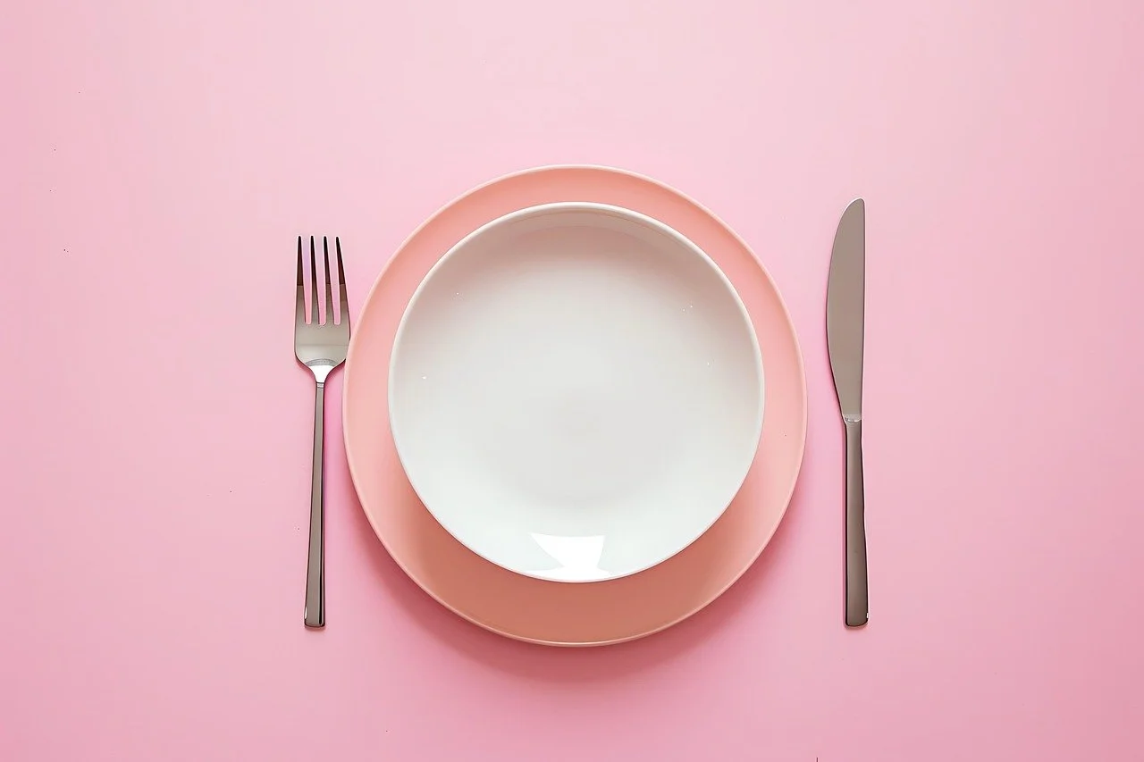 Empty white plate on a pink charger plate, with a fork on the left and a knife on the right, on a pink background. Contact Romero Speech Therapy LLC for help with dysphagia/swallowing difficulty.