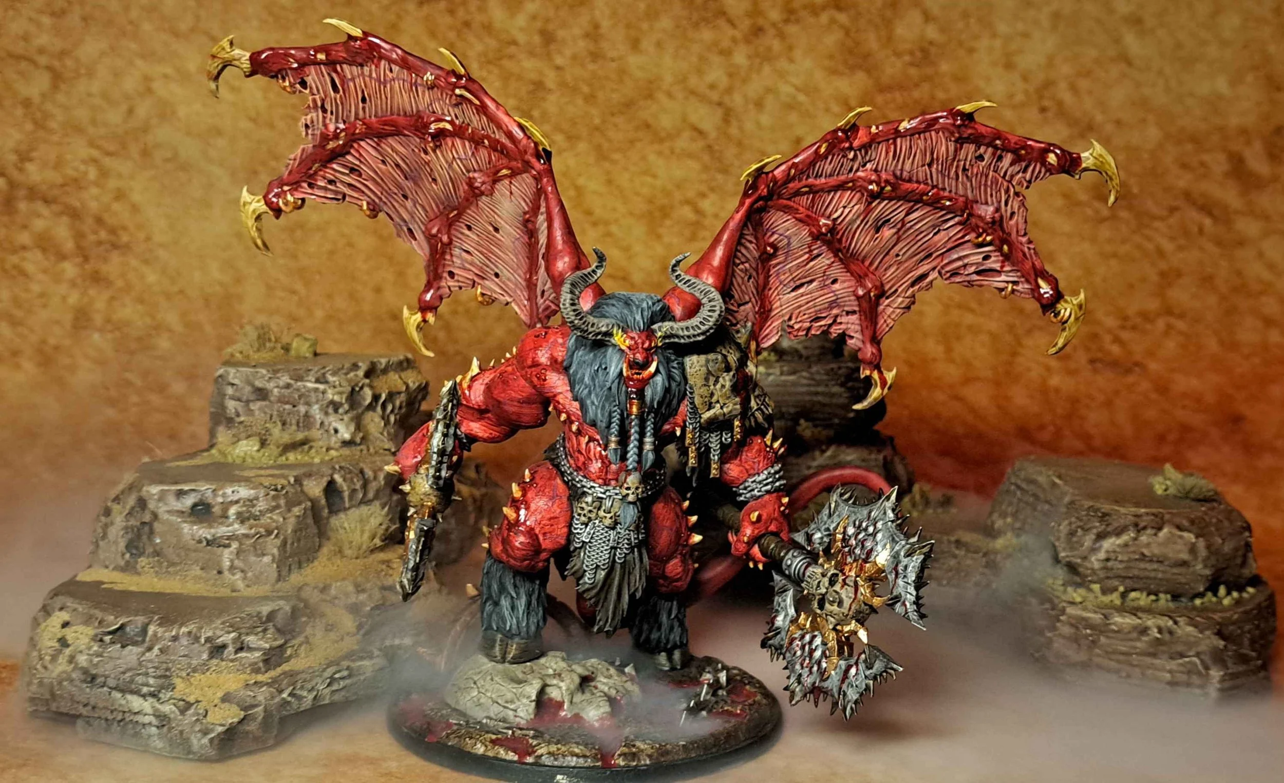 Miniature figure of a demonic creature with large bat-like wings, red skin, black hair, horns, and wearing armor, holding a spiked mace with skulls, set against a rocky background with mist.