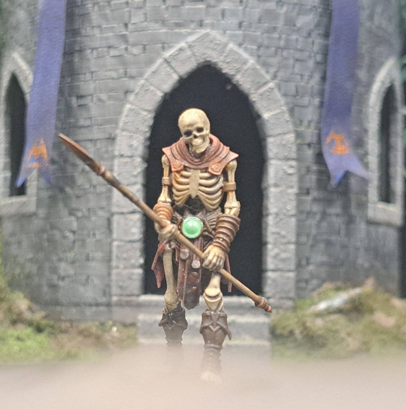A skeleton toy figure dressed as a medieval warrior holding a spear in front of a castle entrance with banners.