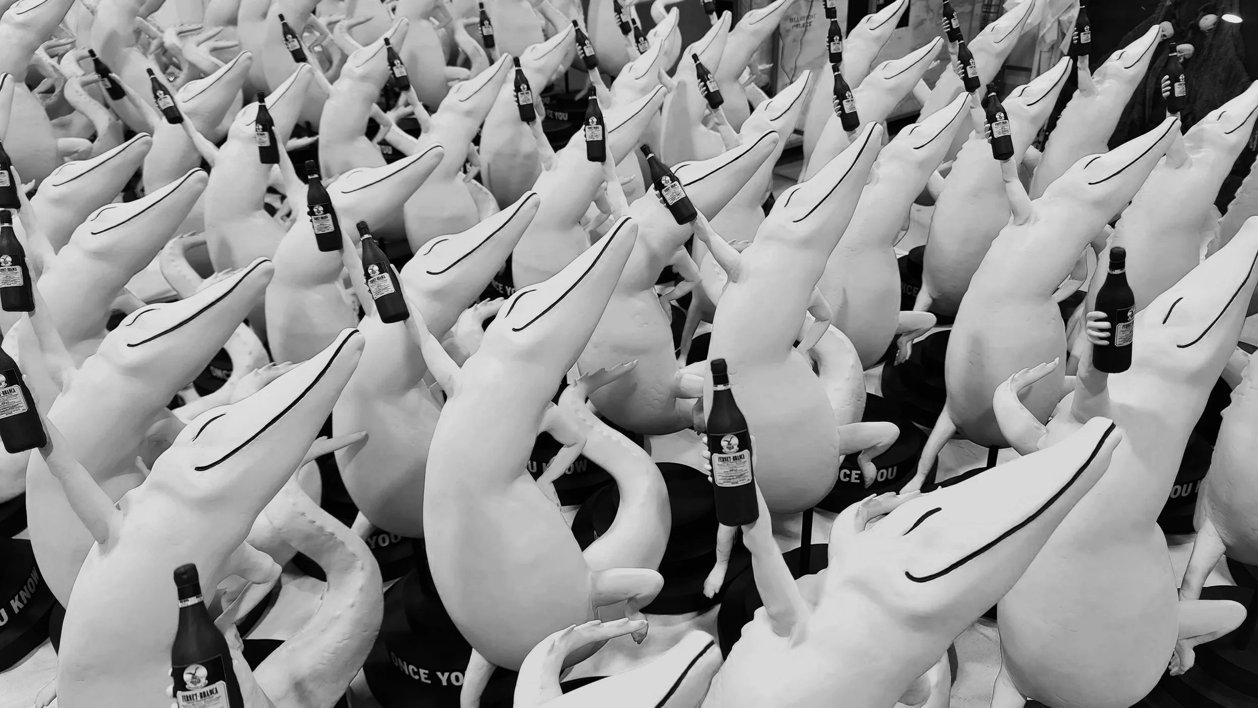 A large collection of plush toy crocodiles, each holding a bottle of beer and wearing a black hat that says 'Once You Know You Know' for Fernet Branca showcasing the mascot, Fernando