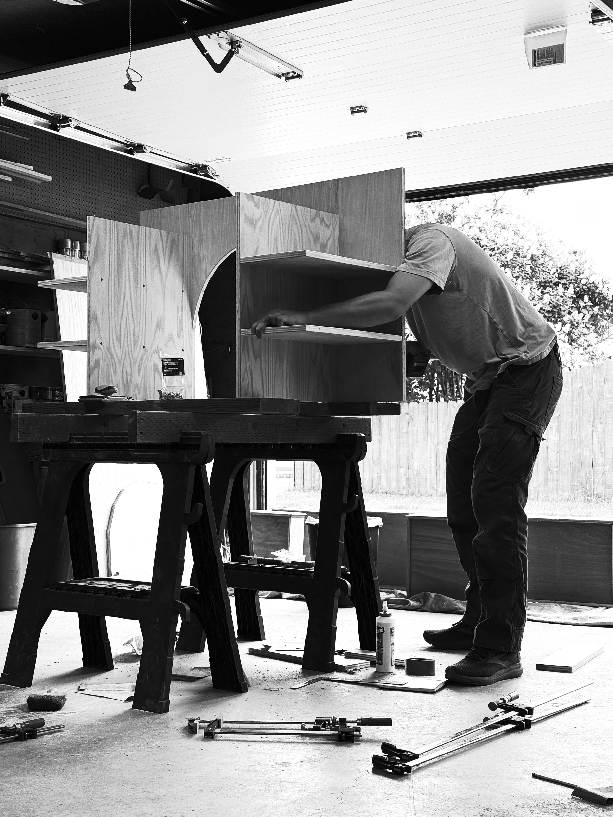 A person assembling a wooden structure in a garage workshop, with tools and construction materials surrounding them.