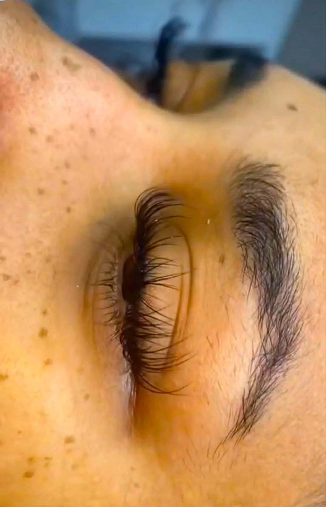 Close-up of a person's eye with long eyelashes, dark eyebrows, and freckles on the cheek.