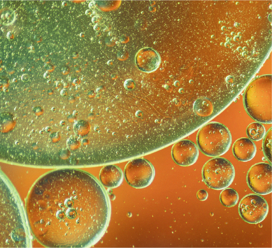 Close-up view of oil droplets in water with green and orange background.