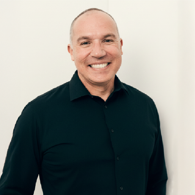 A smiling Dr. Benjamin Flores wearing a black button-up shirt, standing against a plain white wall.