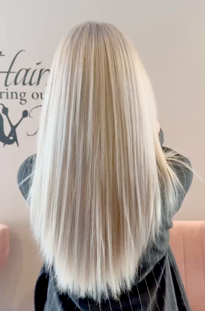 Back view of a woman with long, straight blonde hair in a salon setting.