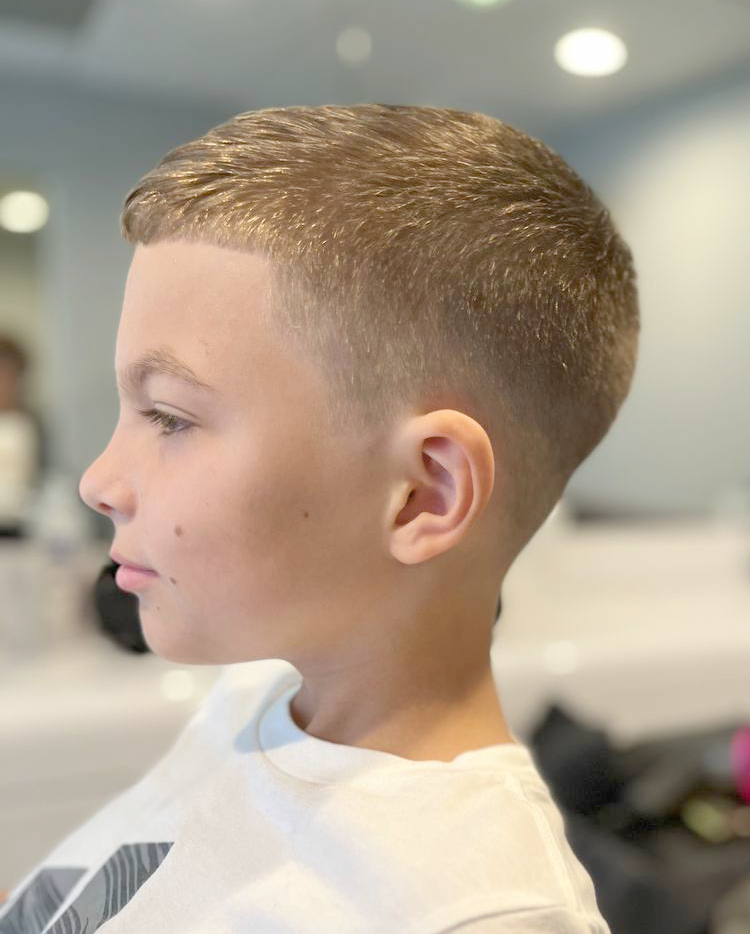 Profile of a young boy with a fresh, high and tight haircut, sitting in a salon or barber shop.