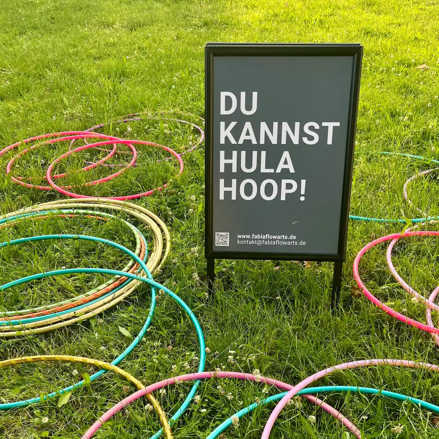 bunte Hula-Hoops auf der Wiese mit Schild "Du kannst Hula-Hoop!"