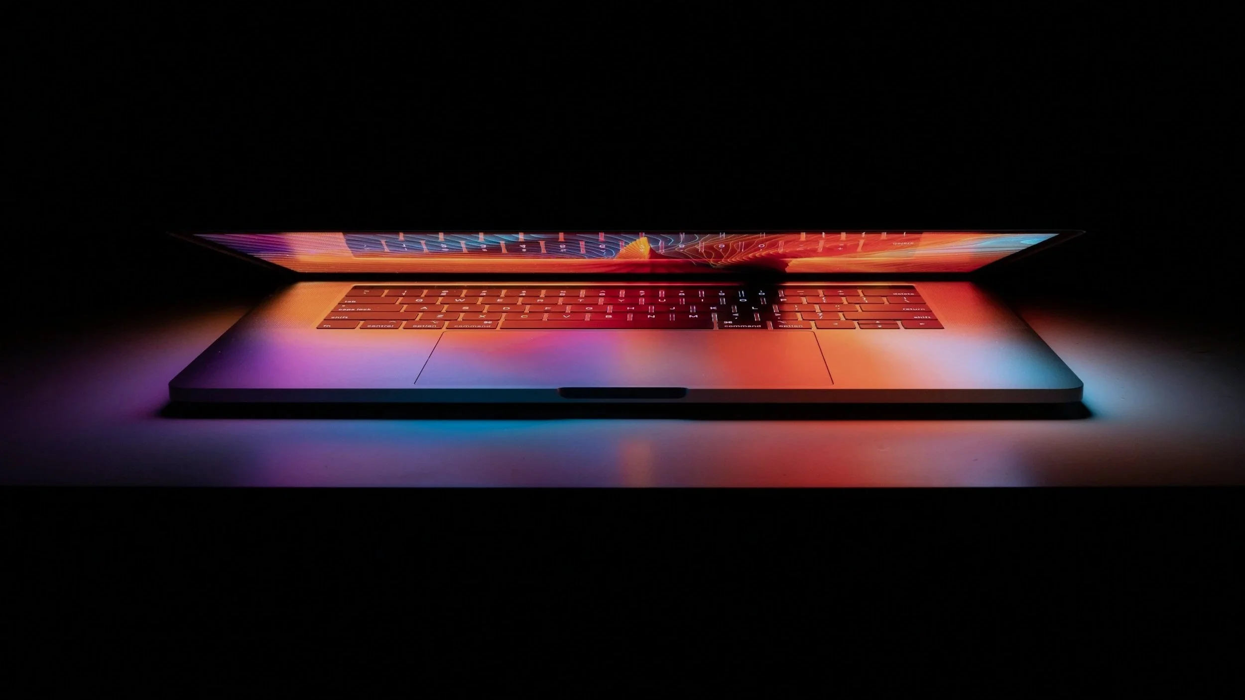 A sleek laptop with a glowing, colorful screen, placed on a dark surface with minimal lighting.
