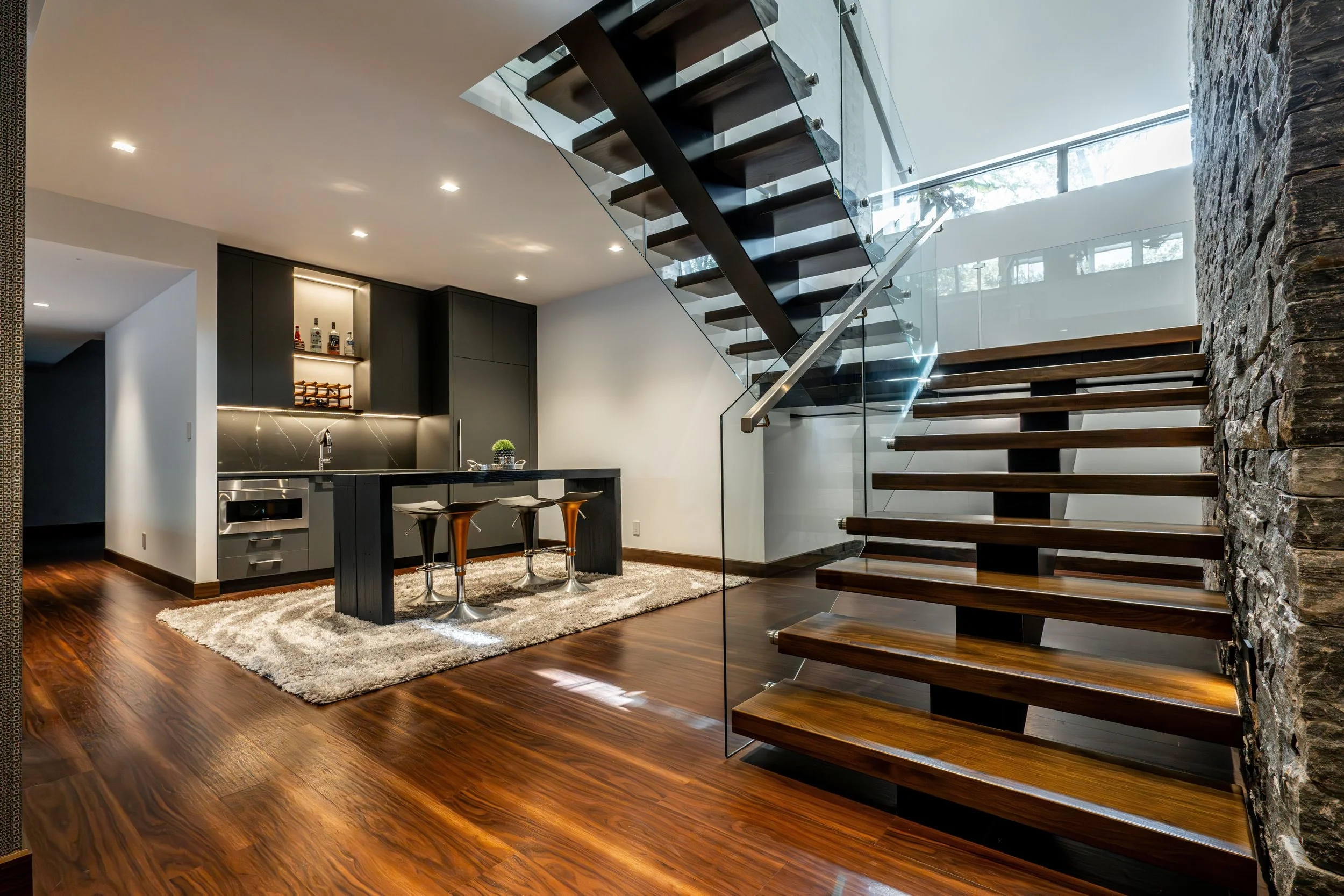 Custom modern interior staircase with steel stringers, wood treads, and glass railing installed in a Winnipeg residential home.