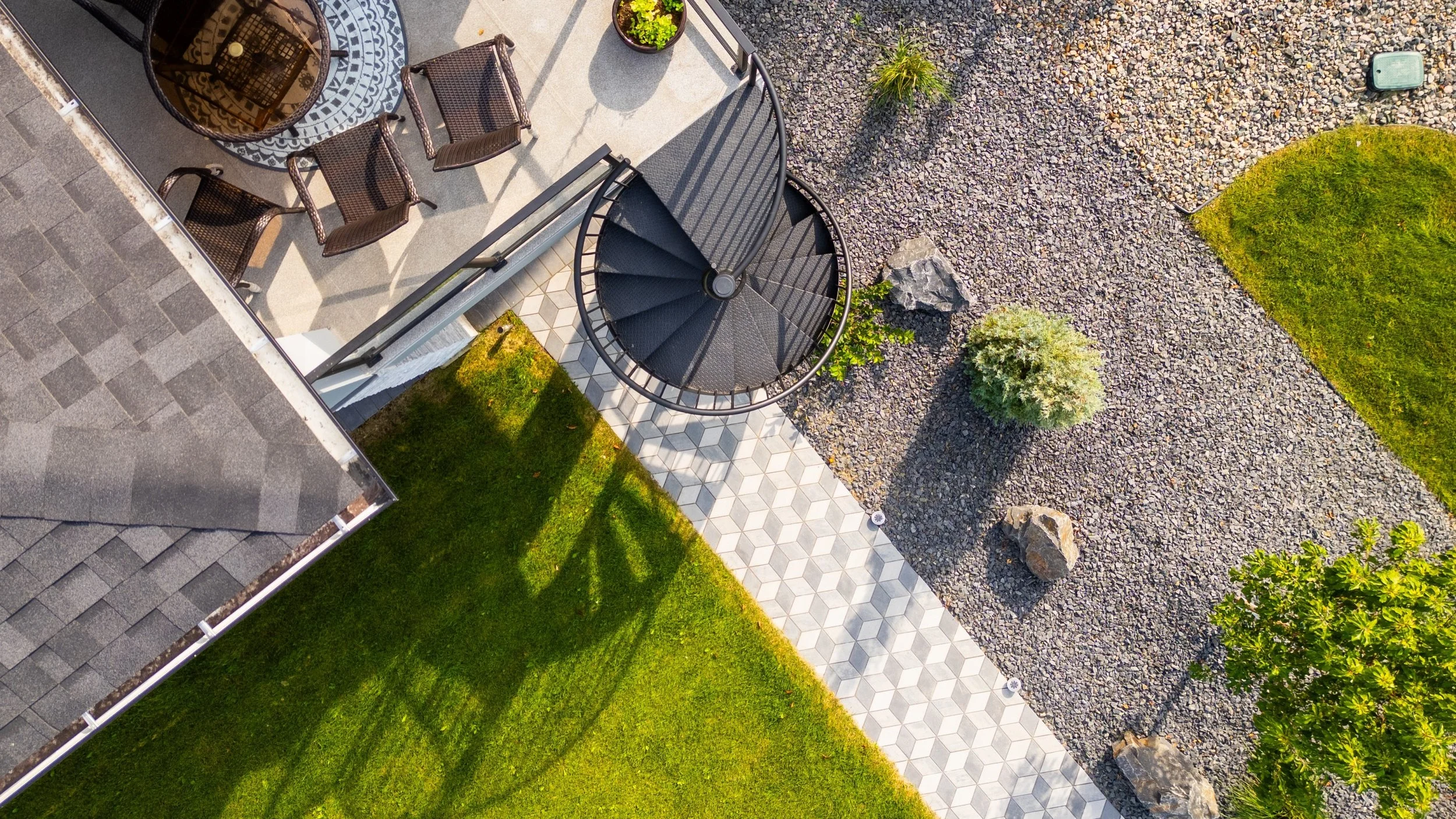Aerial view of a backyard patio with a spiral staircase, outdoor seating, and landscaping including grass, rocks, and small plants.