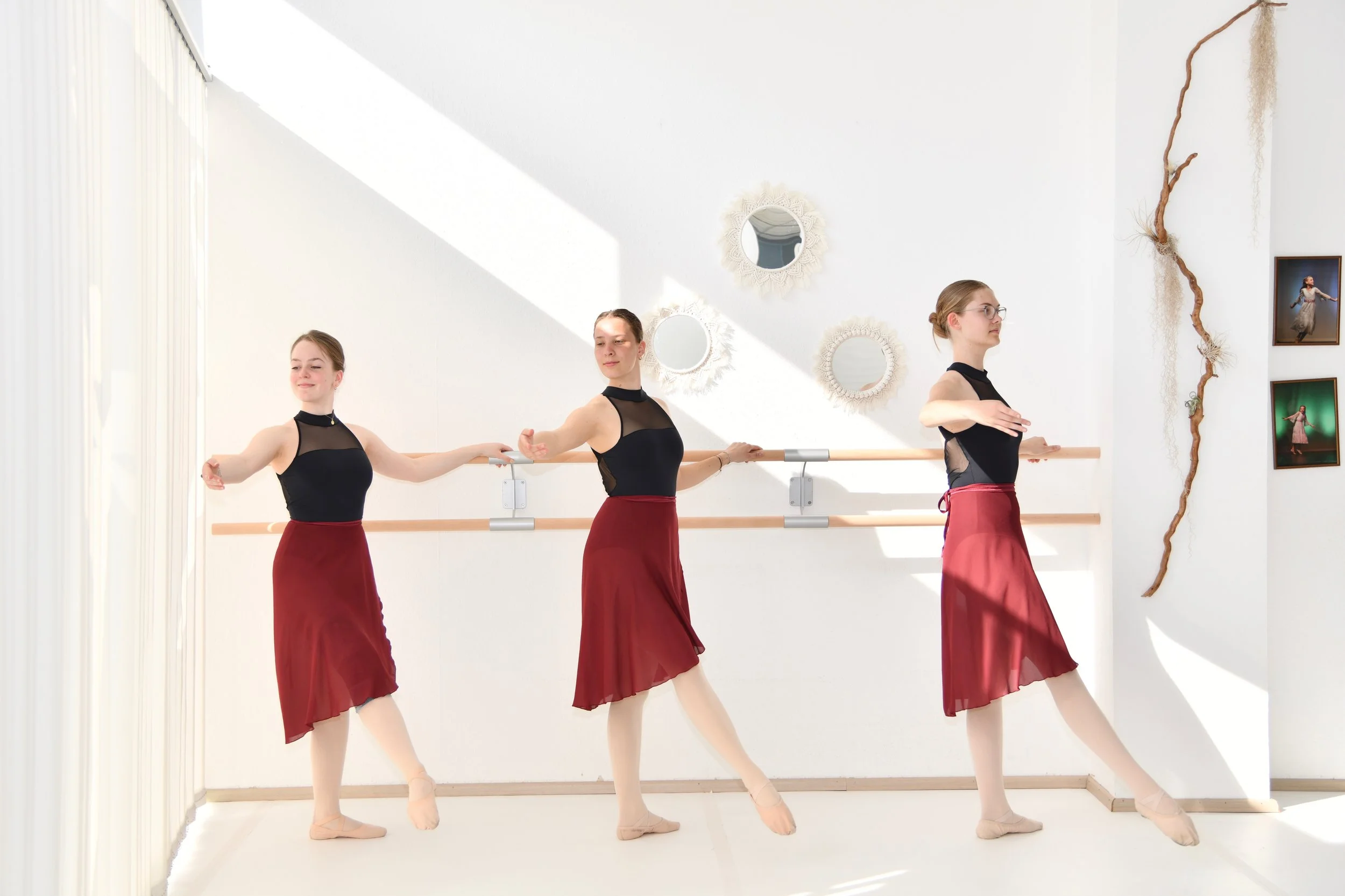 Drei Balletttänzerinnen im Ballettstudio, die eine Choreografie proben, während sie an einer Stange in einer hellen, modern eingerichteten Umgebung tanzen.