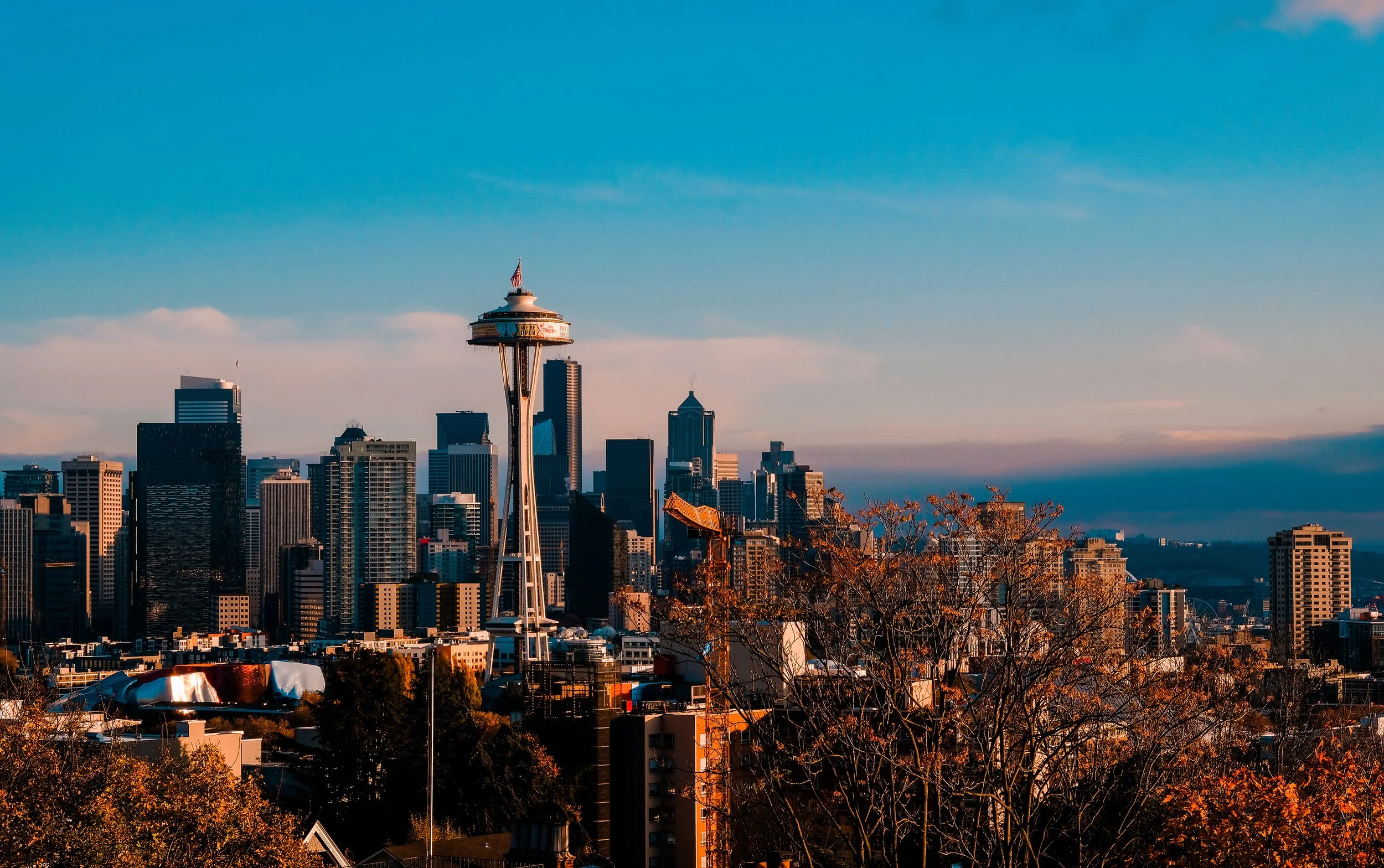 Seattle skyline with the Space Needle in foreground, surrounded by skyscrapers, under a partly cloudy sky during late afternoon.