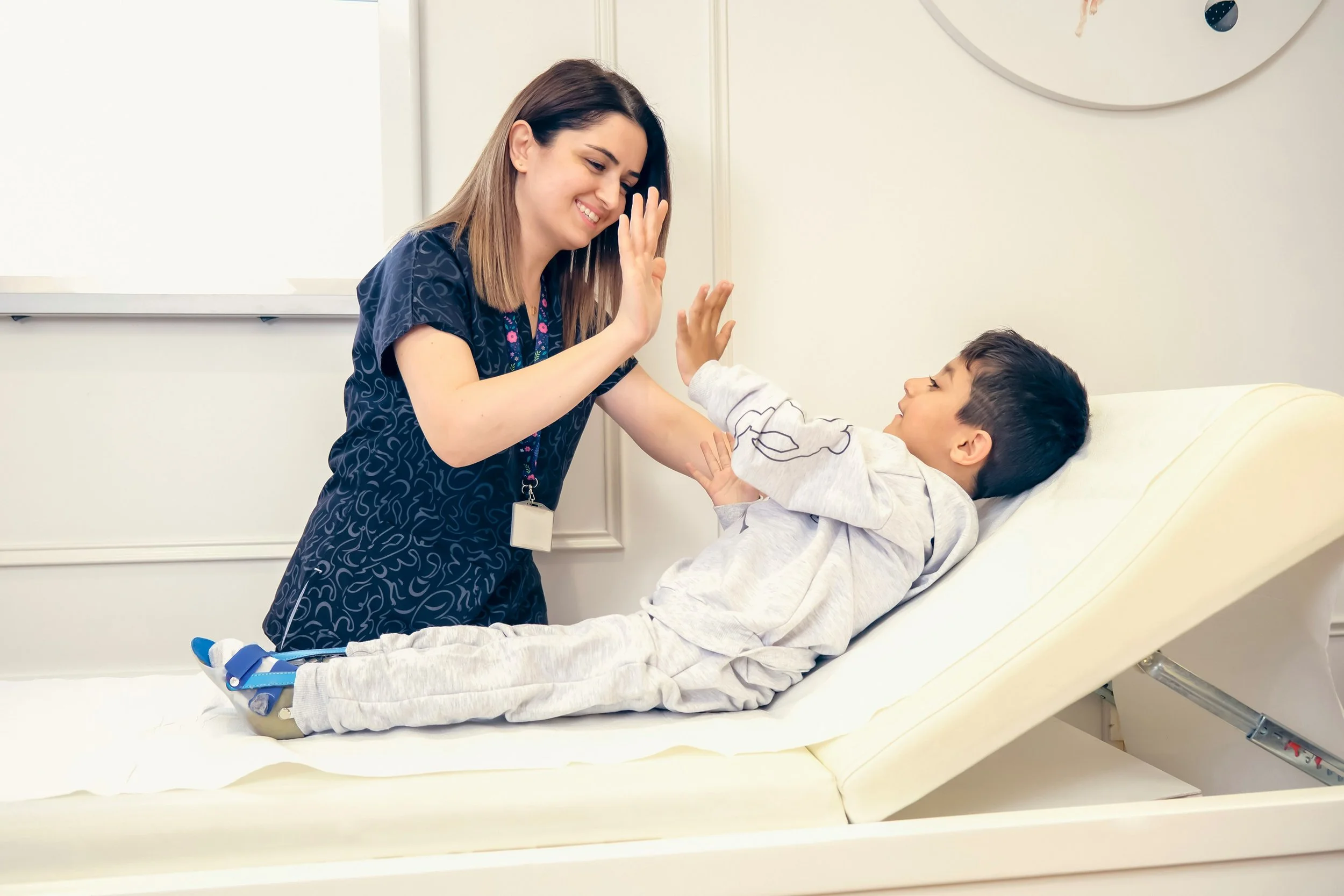 A nurse giving a high five to a young boy lying in a hospital bed.