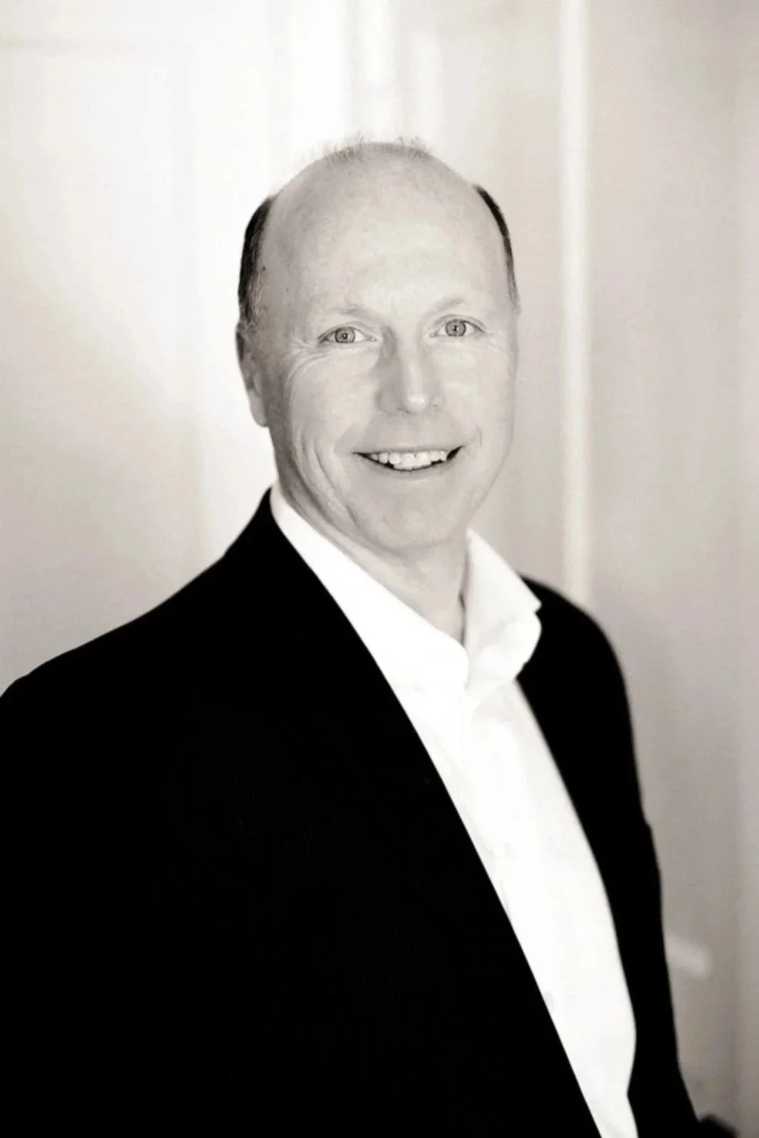 A black and white portrait of a smiling man in a suit and white shirt.